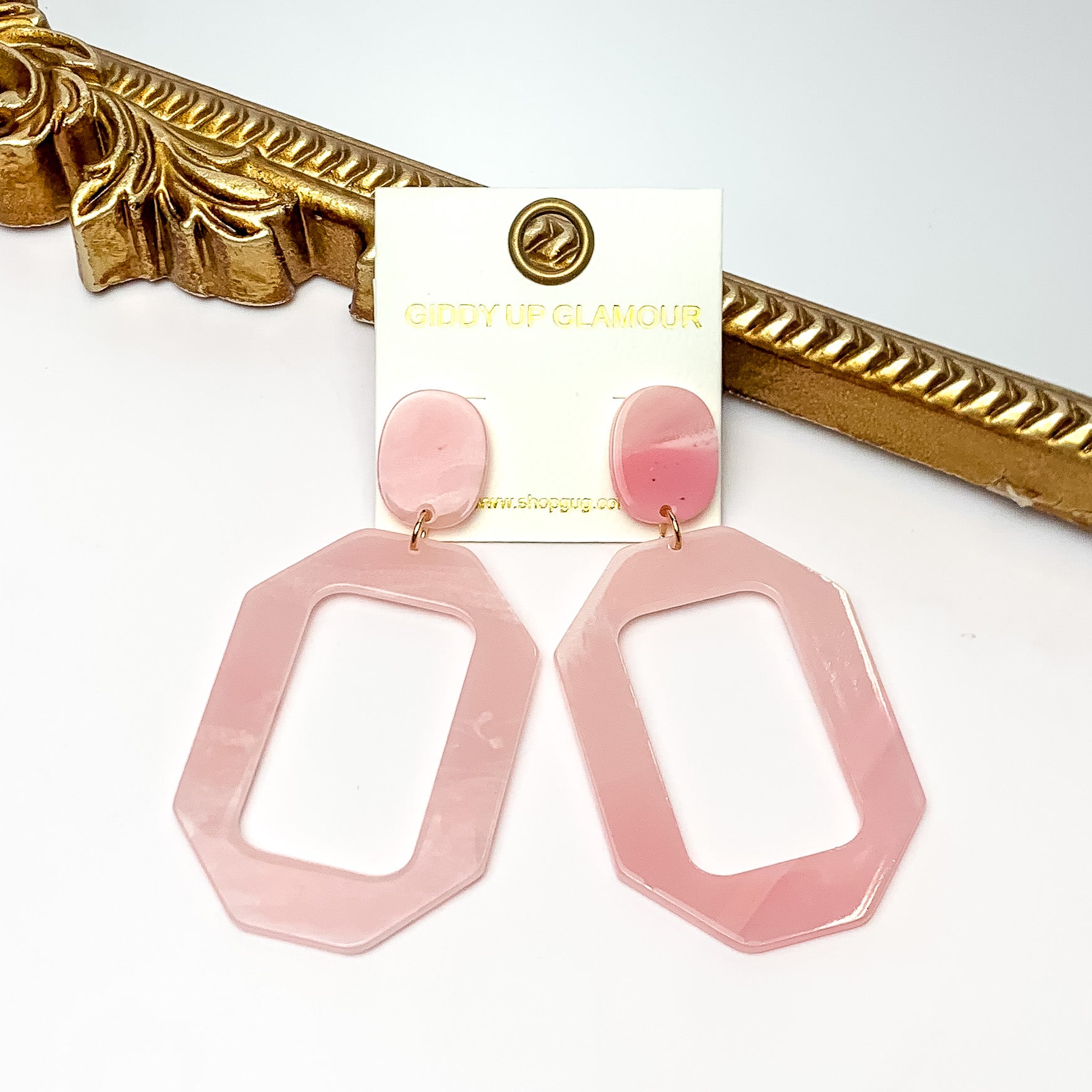 Malibu Marble Open Rectangle Earrings in Light Pink. Pictured on a white background with the earrings laying on a gold frame.
