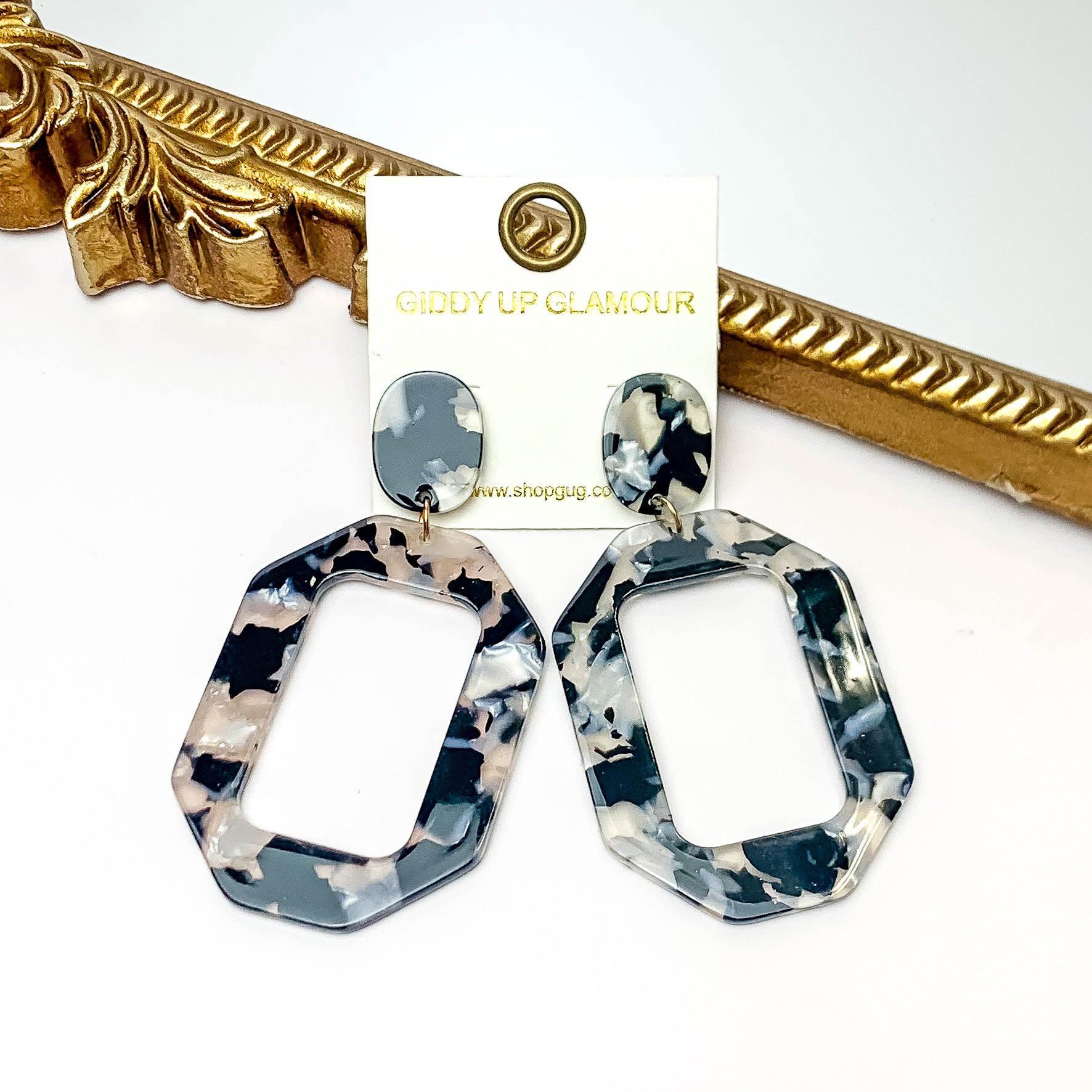 Malibu Marble Open Rectangle Earrings in black. Pictured on a white background with the earrings laying on a gold frame.