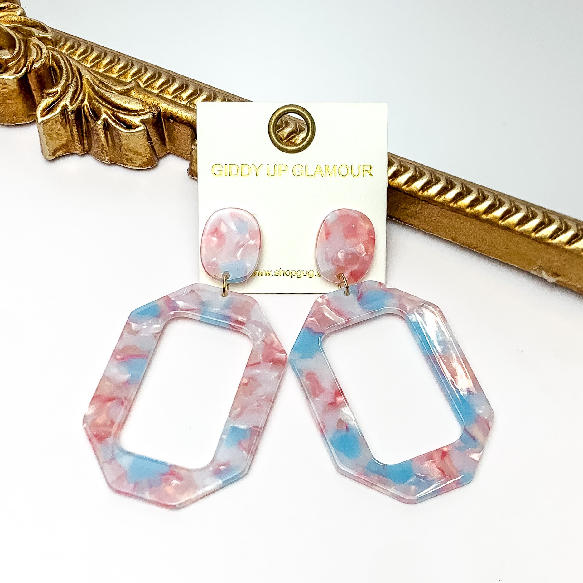 Malibu Marble Open Rectangle Earrings in Pink and Blue. Pictured on a white background with the earrings laying on a gold frame.