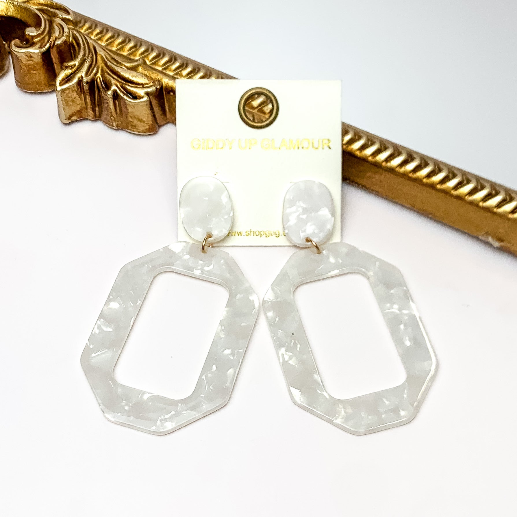 Malibu Marble Open Rectangle Earrings in White. Pictured on a white background with the earrings laying on a gold frame.