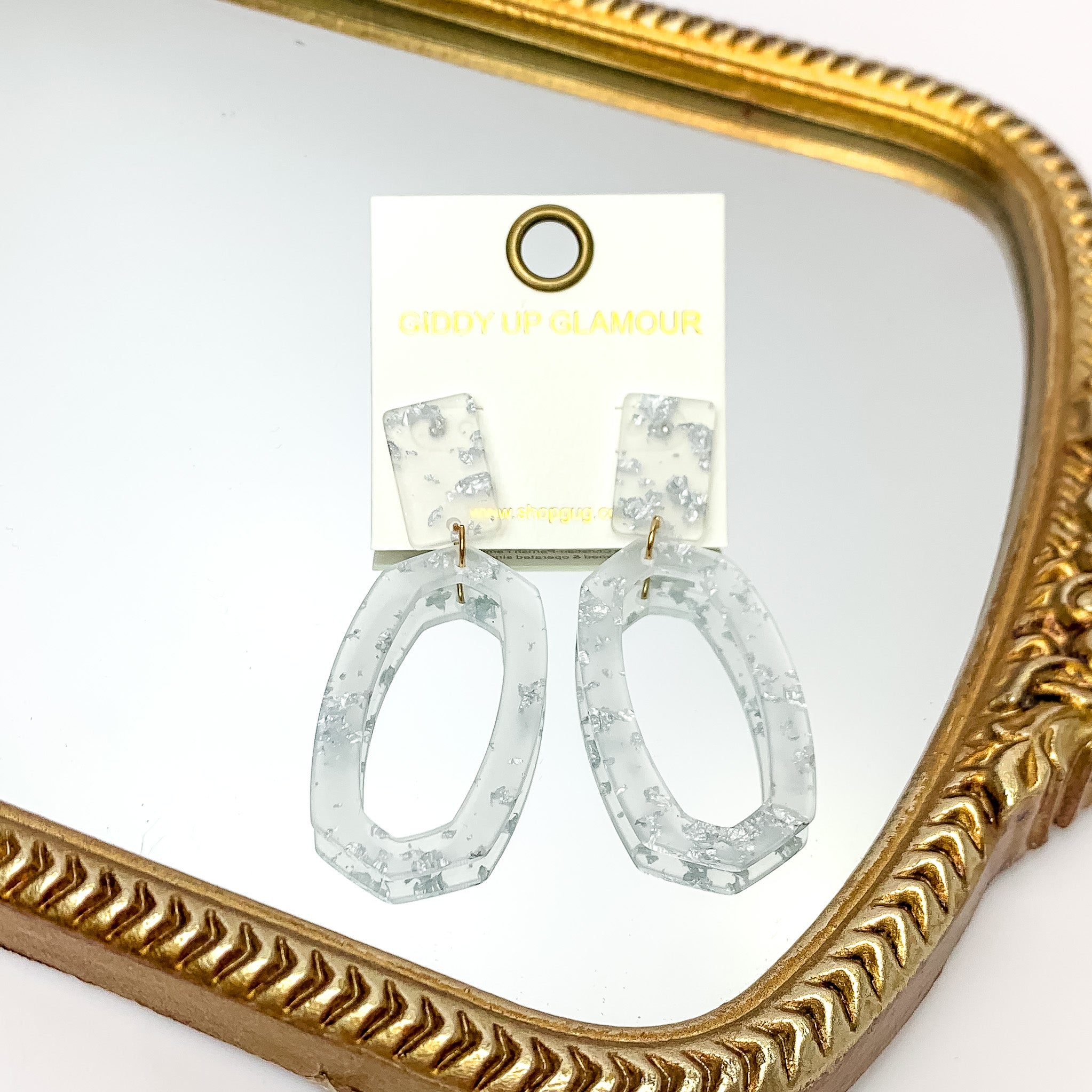 Miami Marble Open Oval Earrings in Clear and Silver. Pictured on a white background with the earrings against a gold frame.