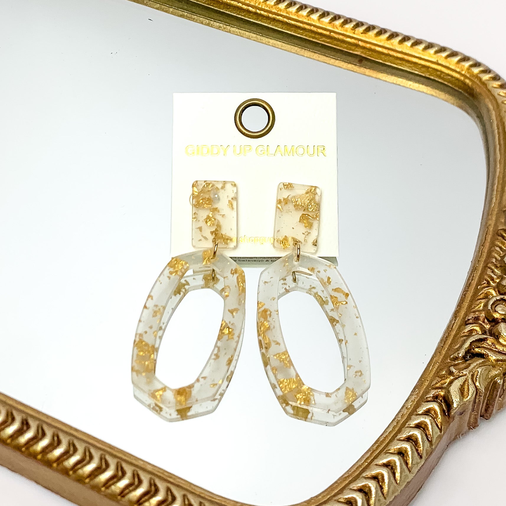Miami Marble Open Oval Earrings in Clear and Gold. Pictured on a white background with the earrings against a gold frame.