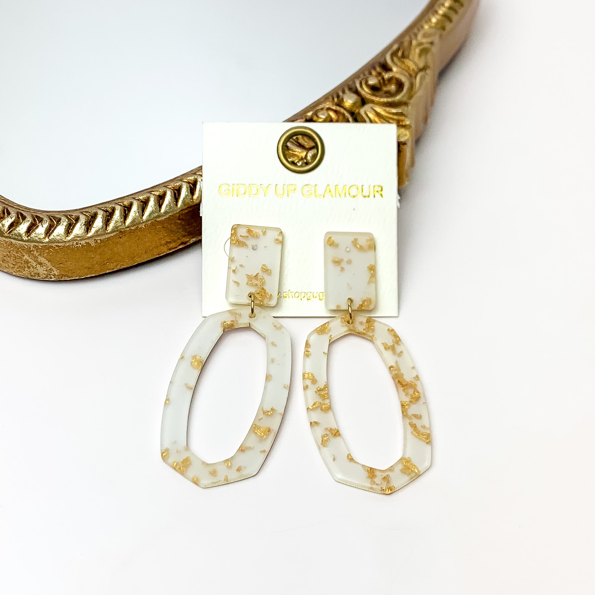 Miami Marble Open Oval Earrings in Cream and Gold. Pictured on a white background with the earrings against a gold frame.