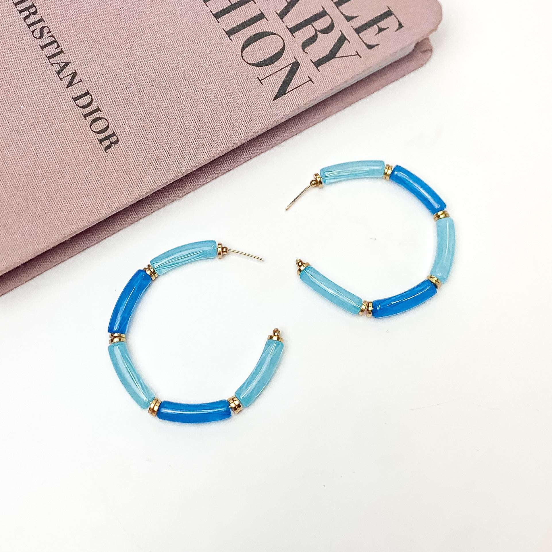 Island Style Tube Beaded Hoop Earrings Blue. Pictured on a white background with a book in the top left corner.