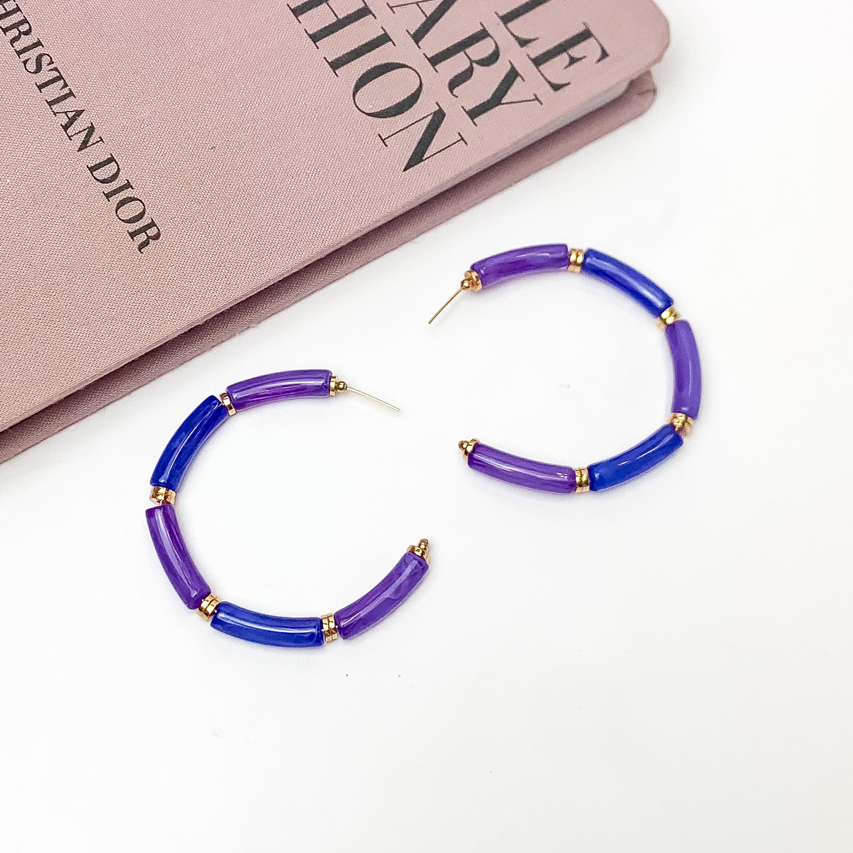 Island Style Tube Beaded Hoop Earrings Purple. Pictured on a white background with a book in the top left corner.