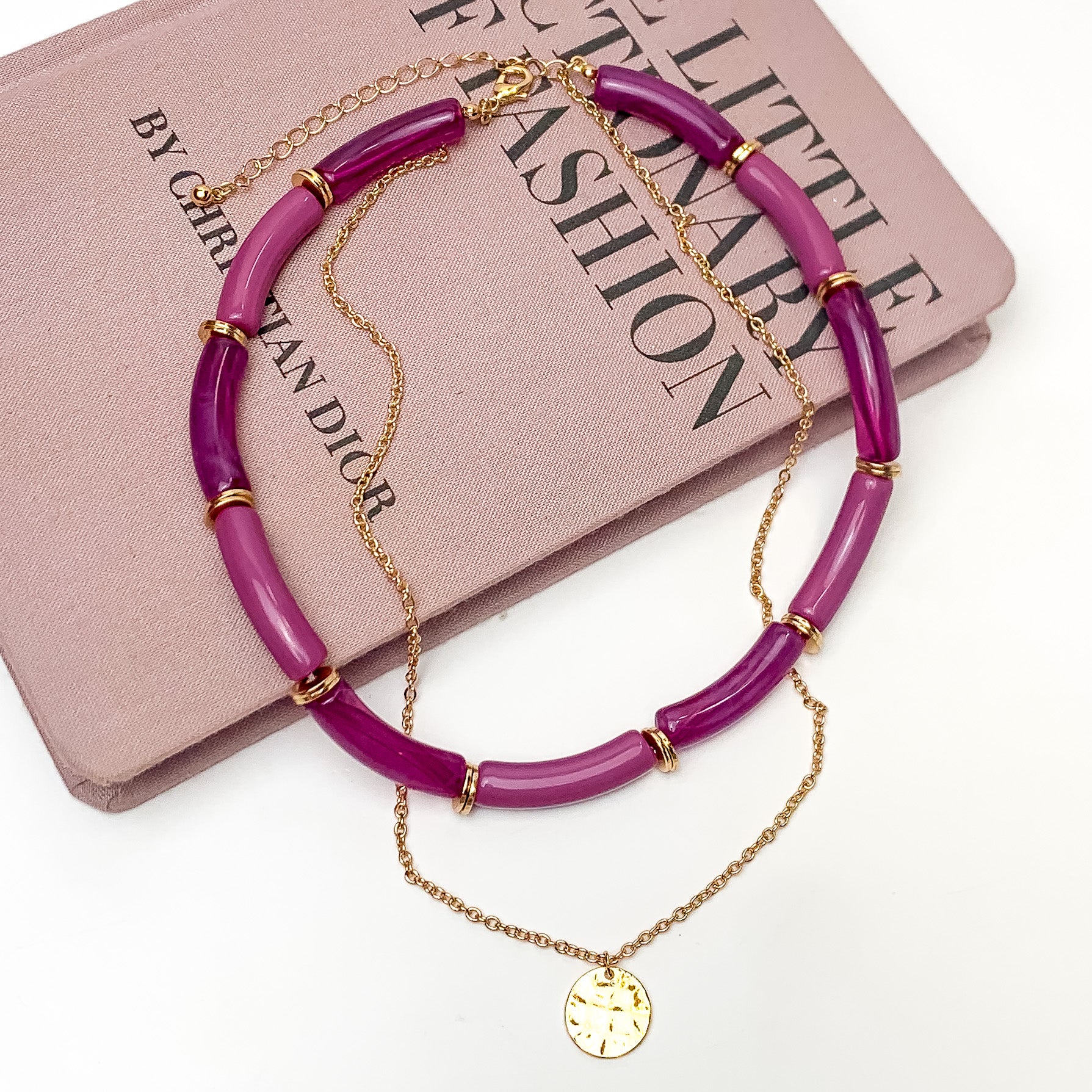 Perfect Paradise Tube Necklace With Second Gold Tone Chain Necklace In Purple. Pictured on a white background with the necklace laying on a book.