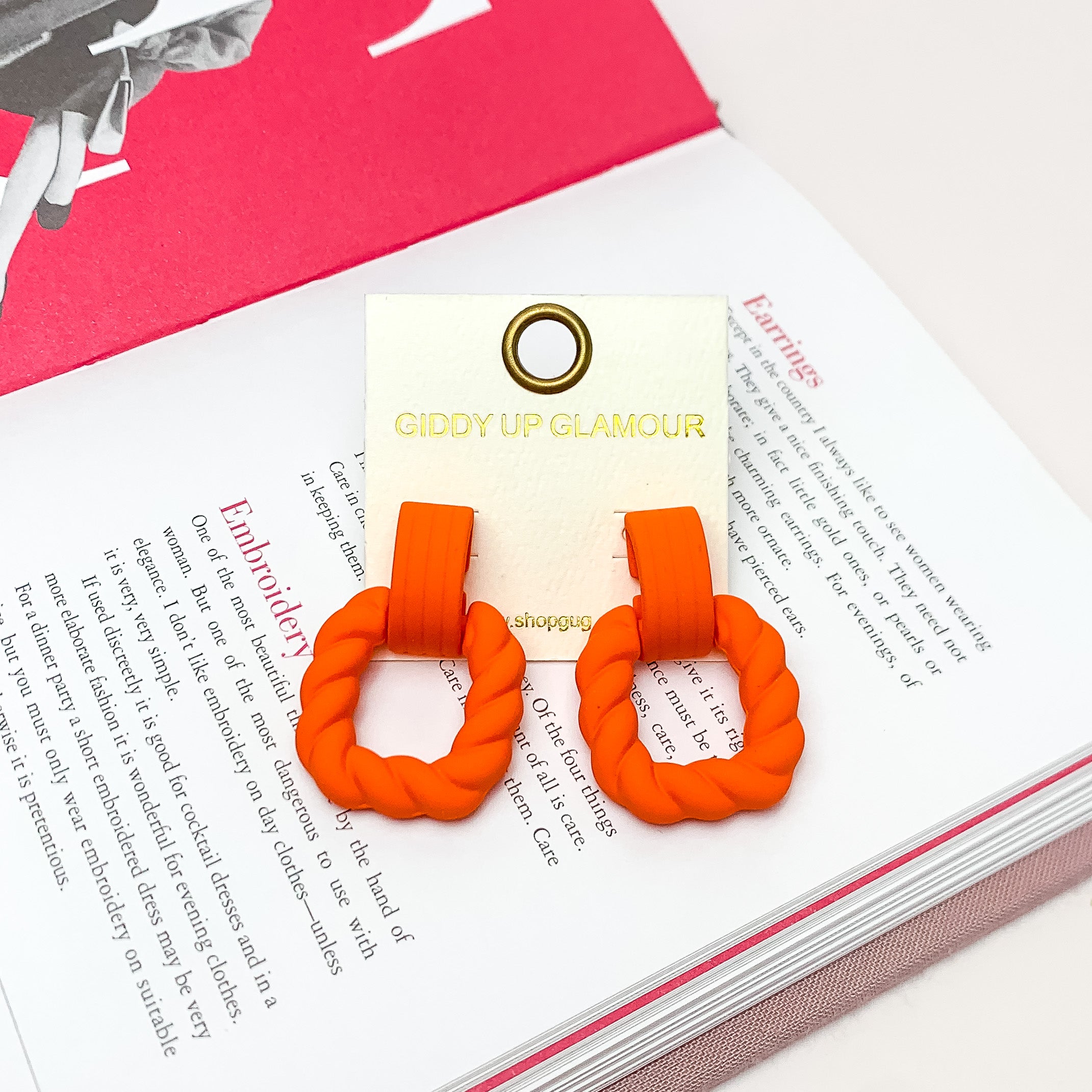 Ready to Party Twisted Square Earrings in Orange. Pictured on an open page of a book.