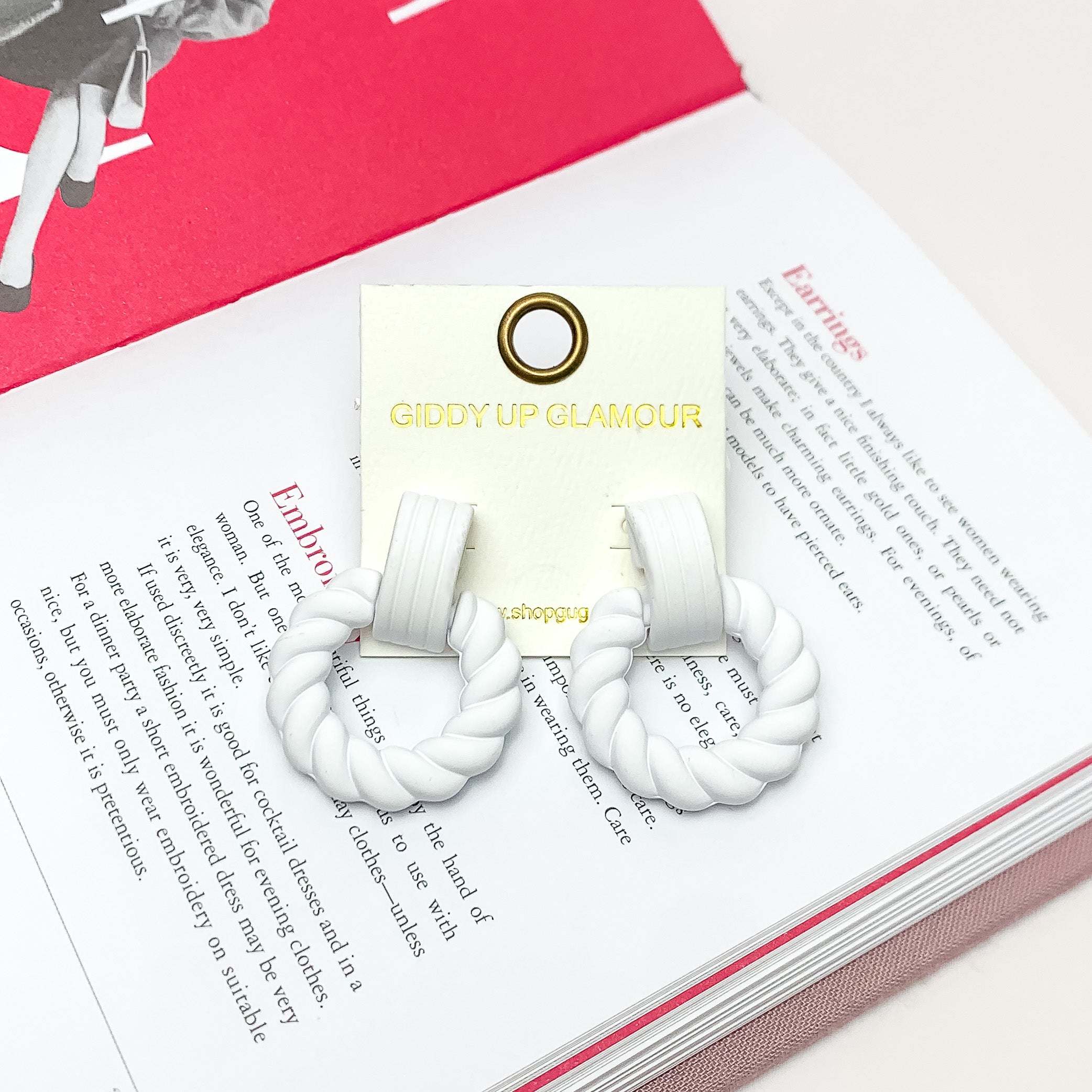 Made to Party Twisted Circle Earrings in White. Pictured on an open page of a book.