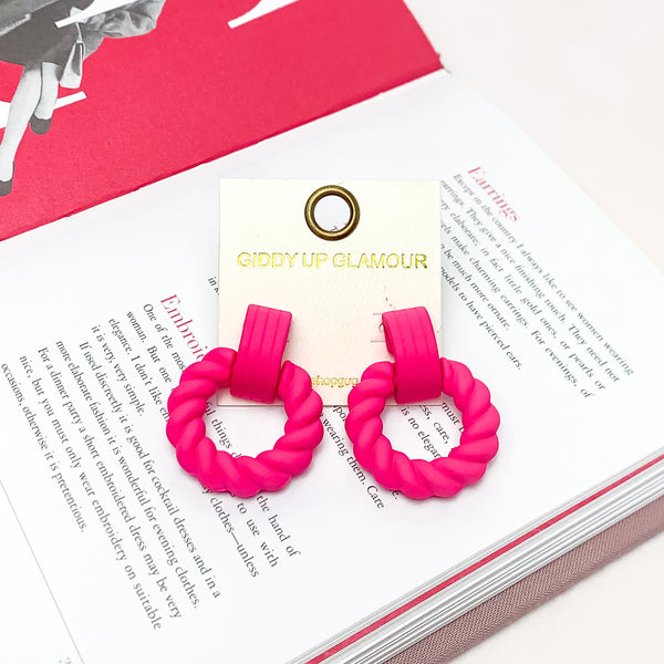 Made to Party Twisted Circle Earrings in Hot Pink. Pictured on an open page of a book.