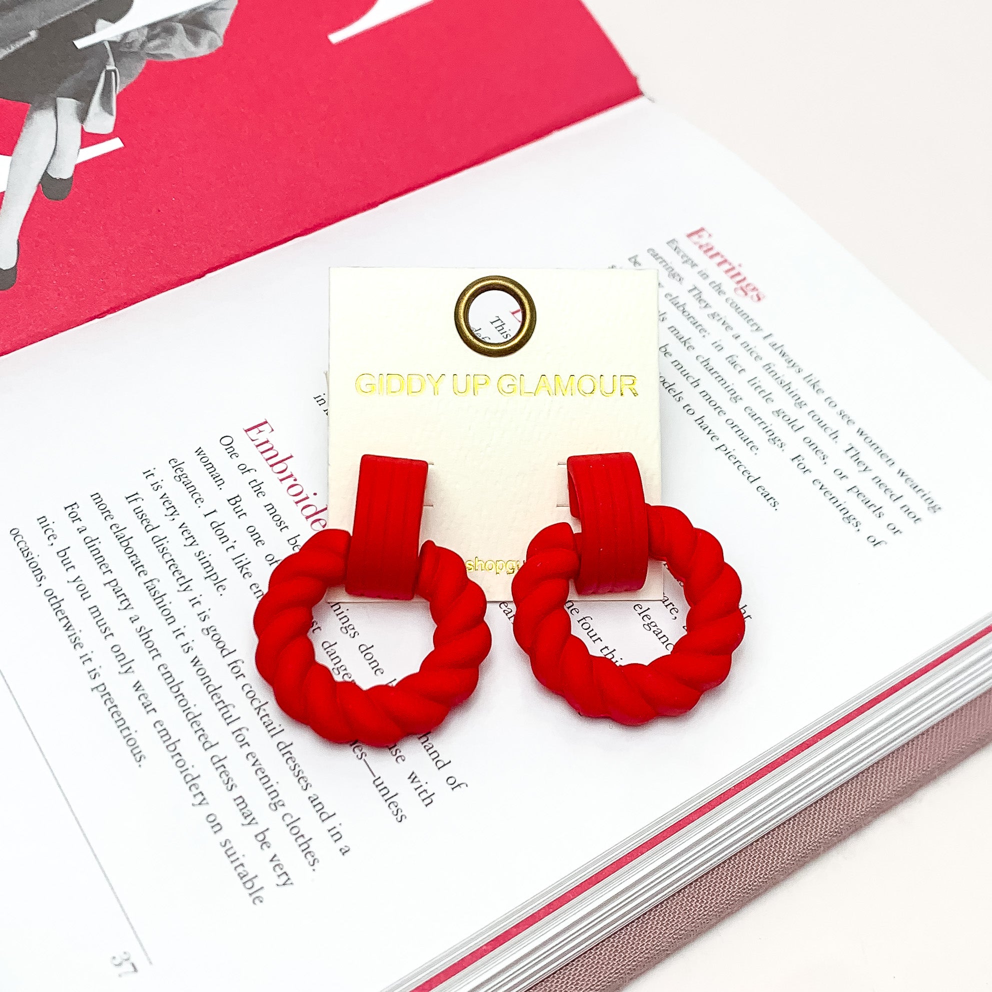 Made to Party Twisted Circle Earrings in Red. Pictured on an open page of a book.