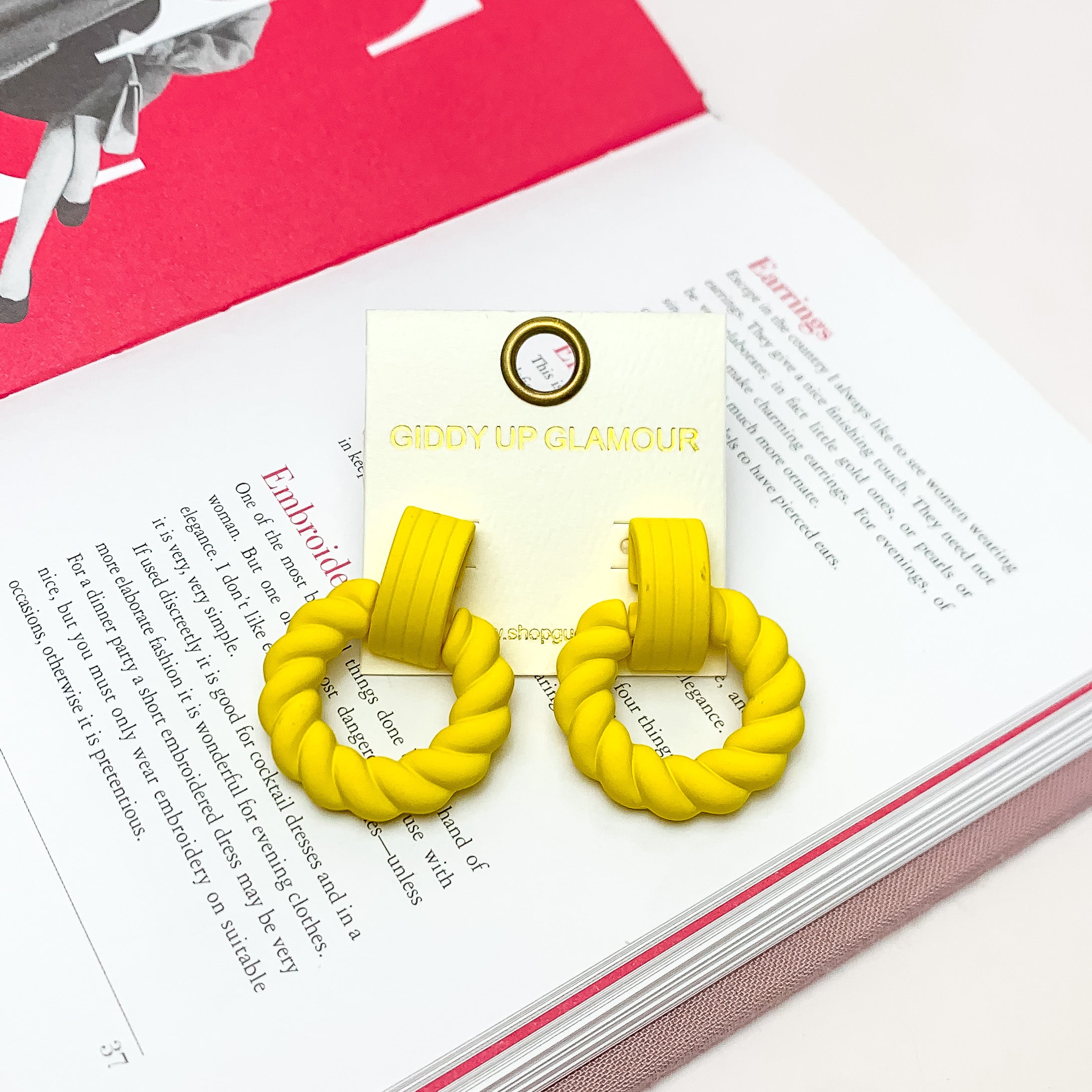 Made to Party Twisted Circle Earrings in Yellow. Pictured on an open page of a book.