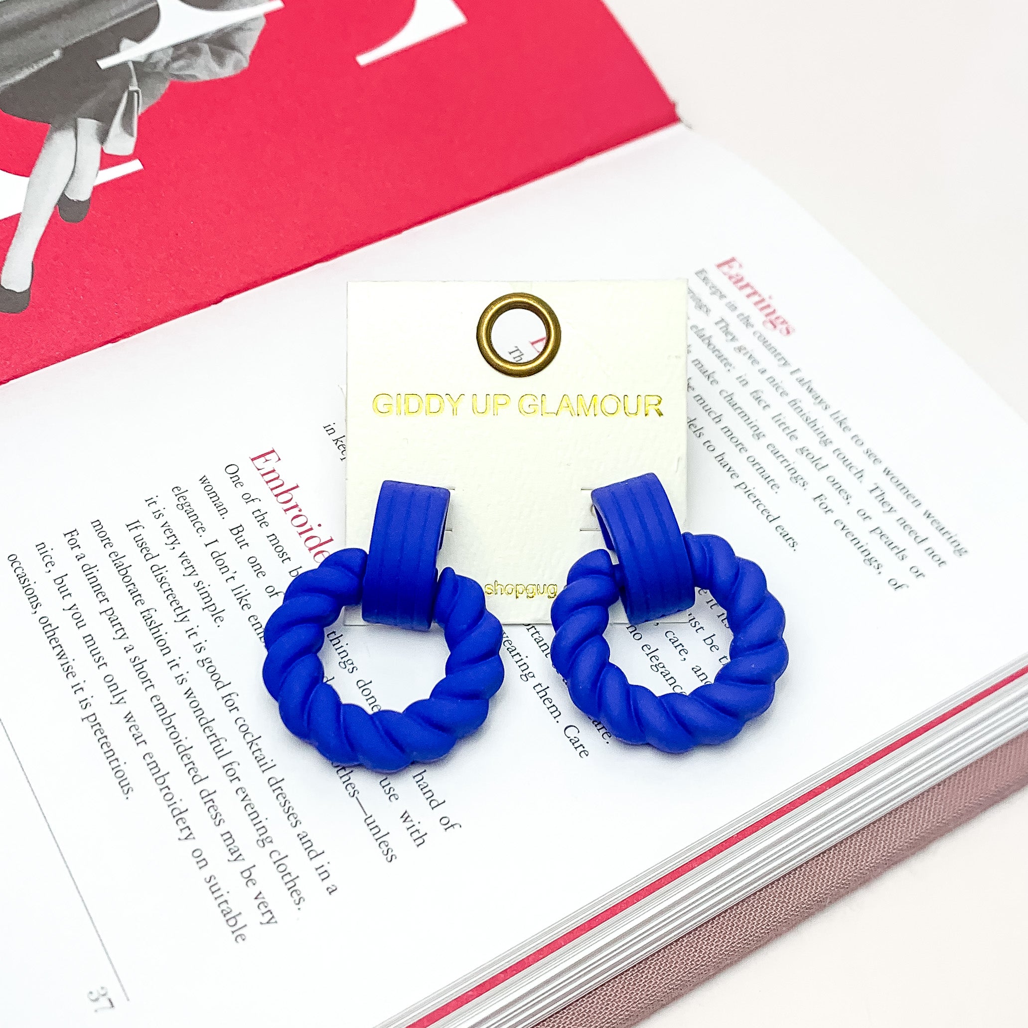 Made to Party Twisted Circle Earrings in Royal Blue. Pictured on an open page of a book.