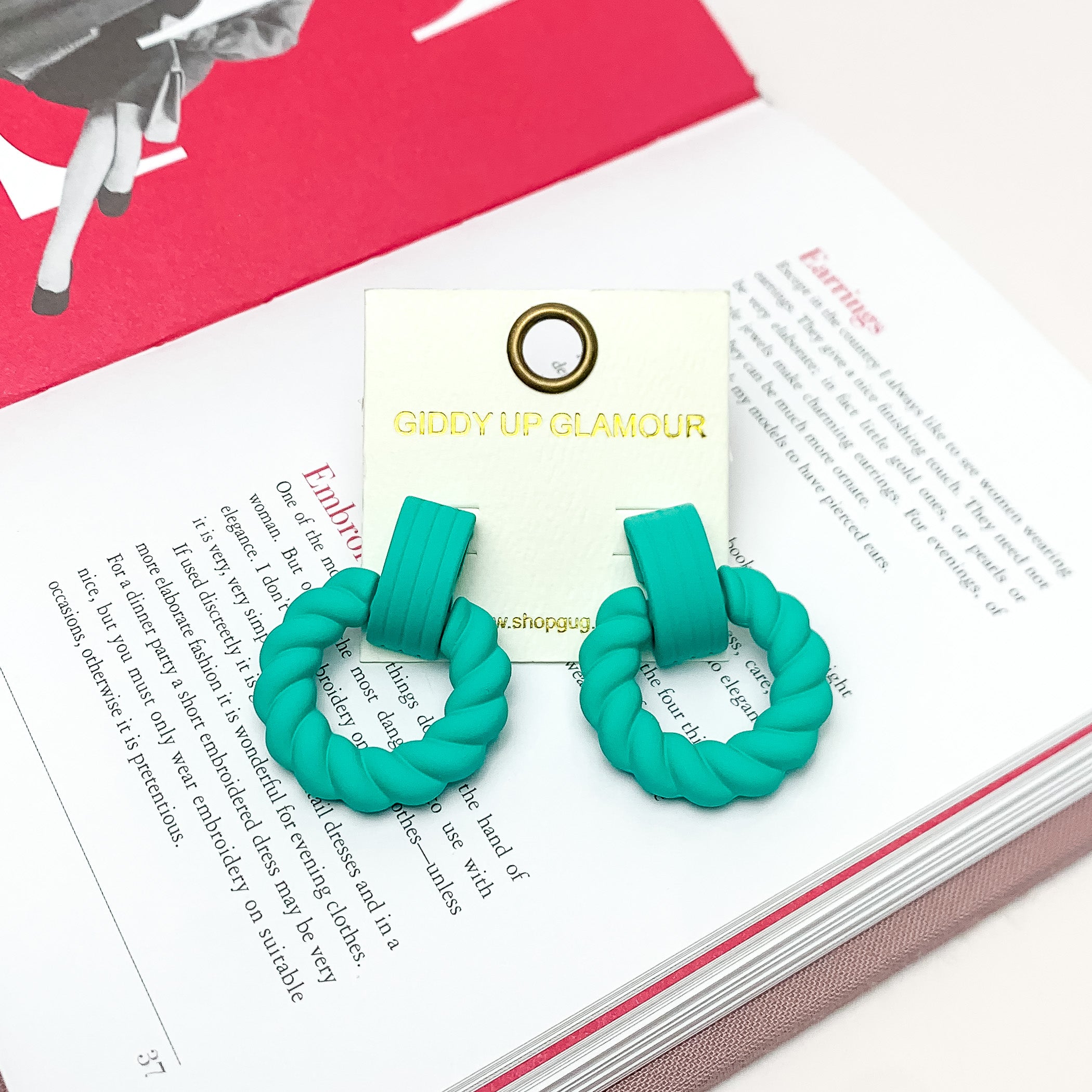 Made to Party Twisted Circle Earrings in Mint Green. Pictured on an open page of a book.
