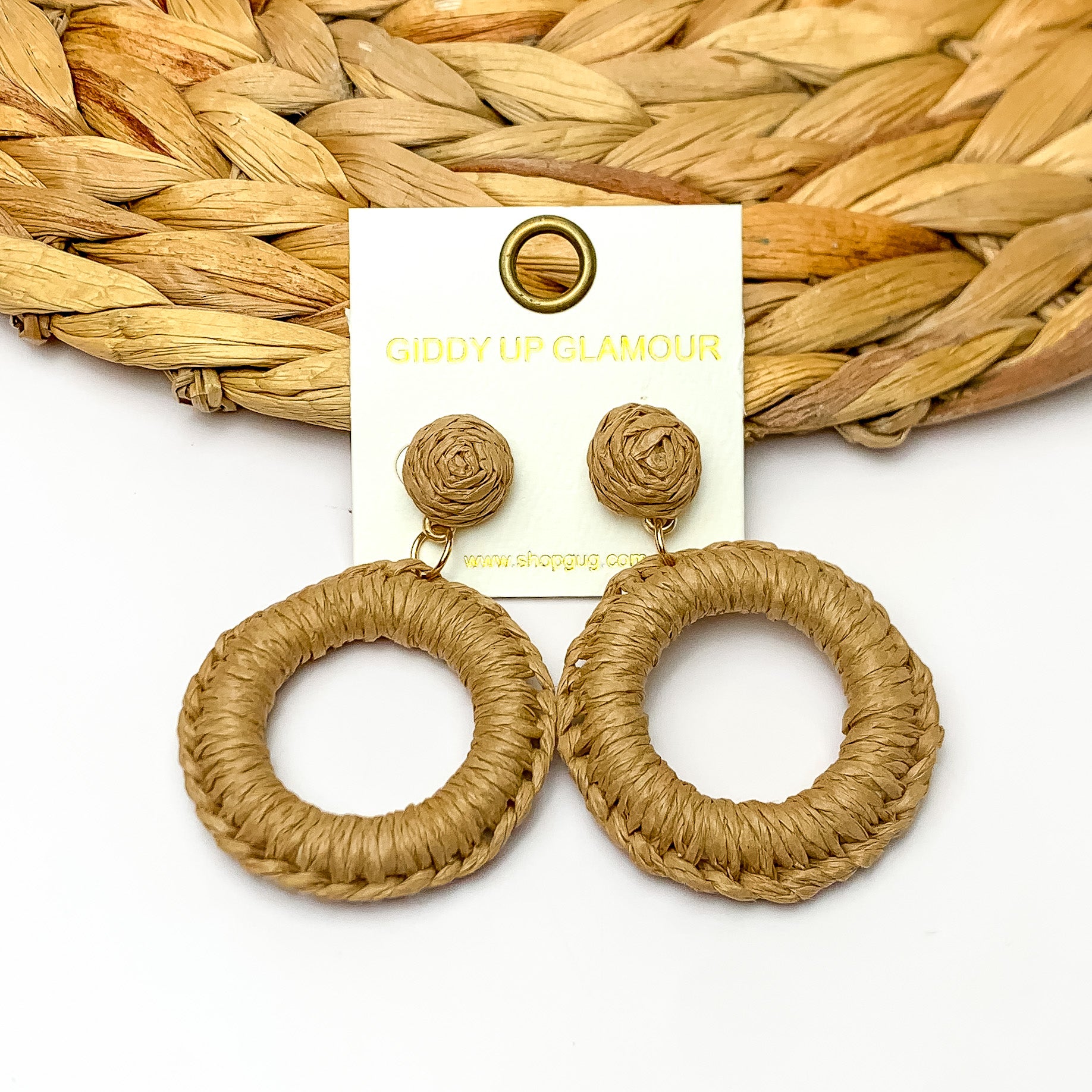 Beachside Café Raffia Wrapped Circle Earrings in Brown. Pictured on a white background with the top of the earrings laying on a brown circle decorative piece.
