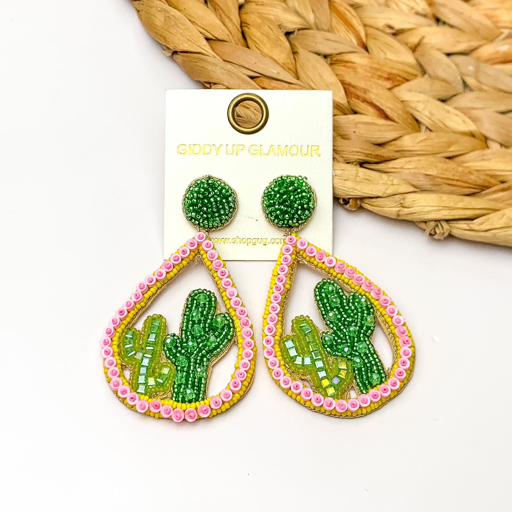 Beaded Open Teardrop Earrings With Cactus Scene on the Inside in Light Pink. Pictured on a white background with a wood piece decoration in the top right corner.