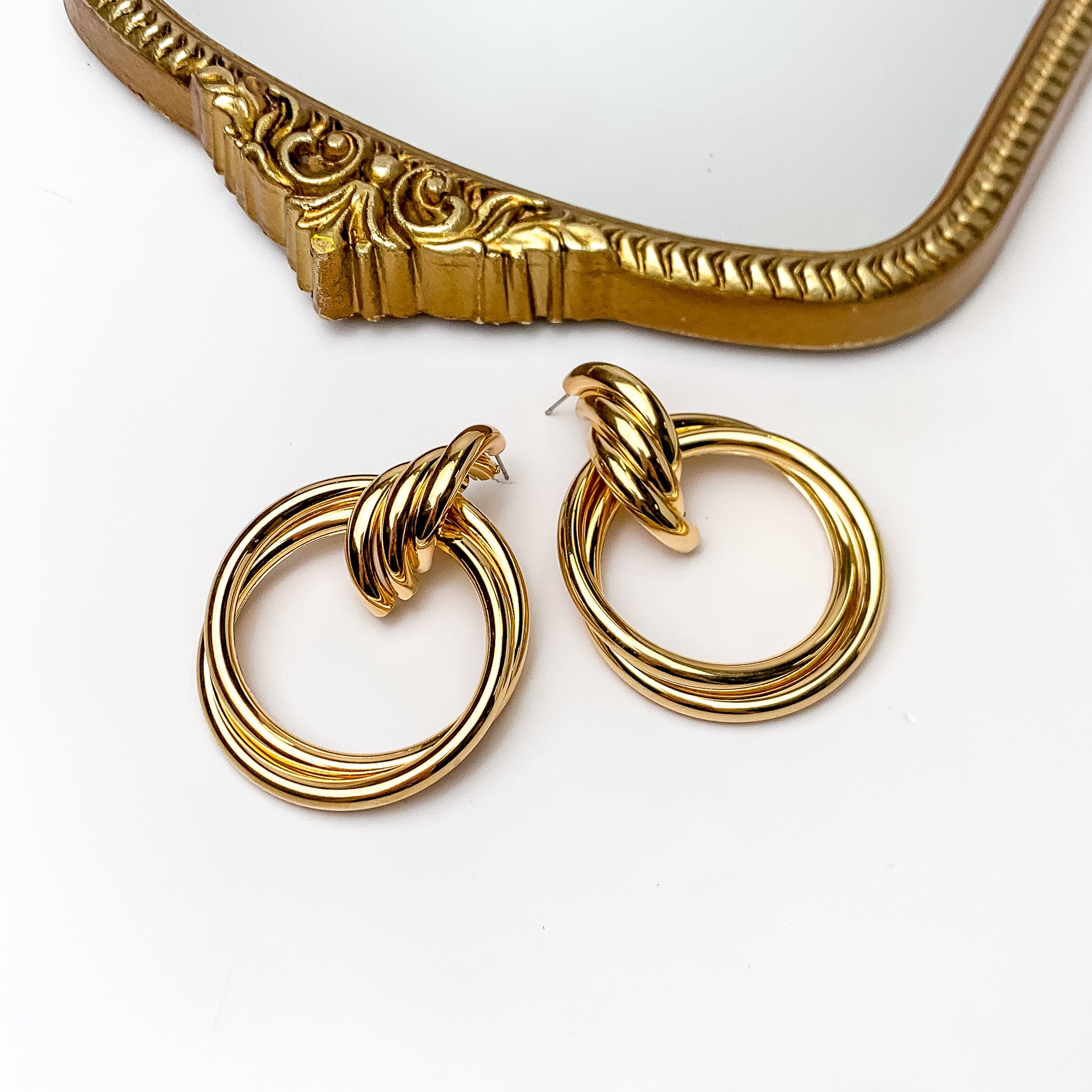 Gold Tone Large Twisted Post Circle Earrings. Pictured on a white background with a gold frame above the earrings.