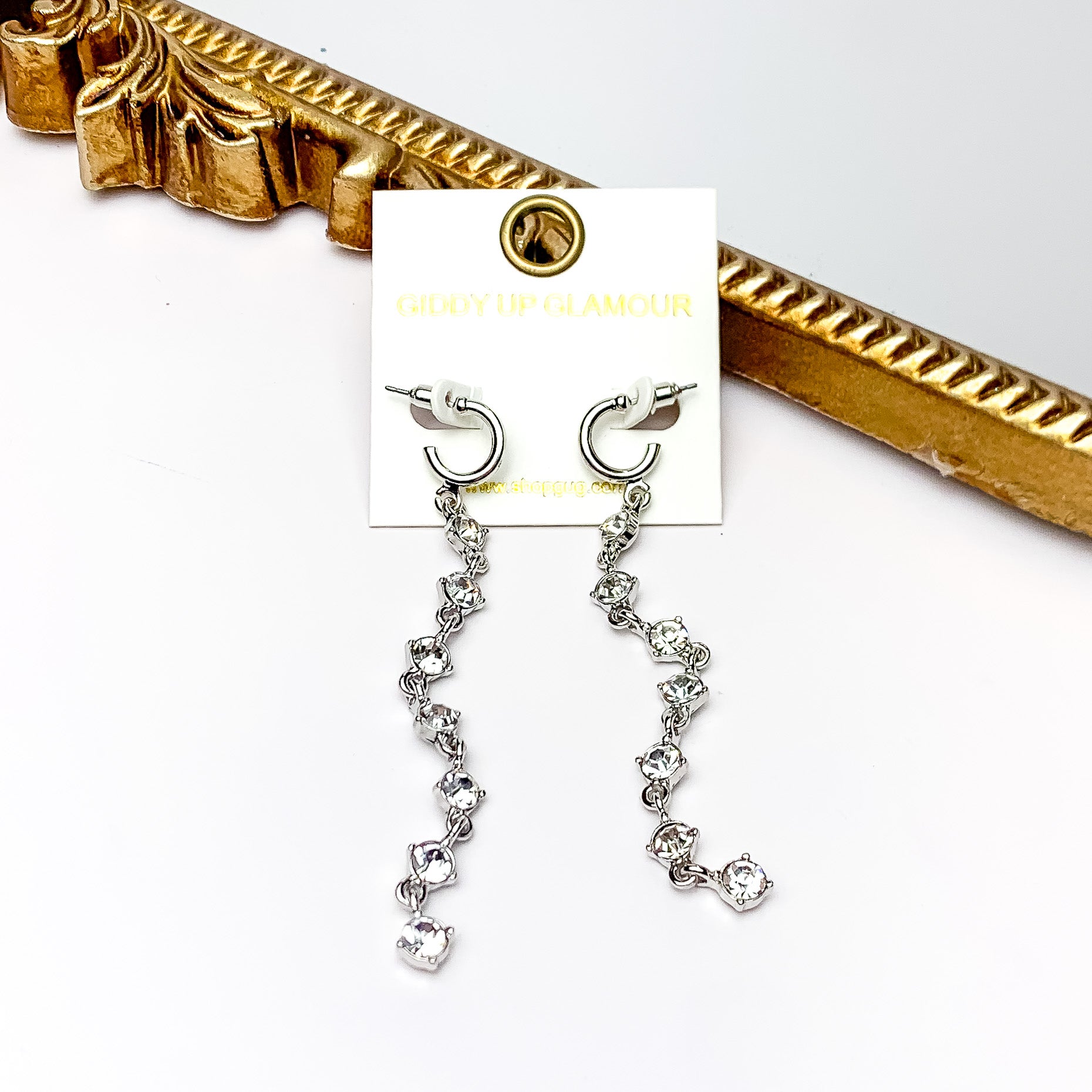 Red Carpet Moment Long Silver Tone Earrings With Clear Crystals. Pictured on a white background with a gold frame behind the earrings.