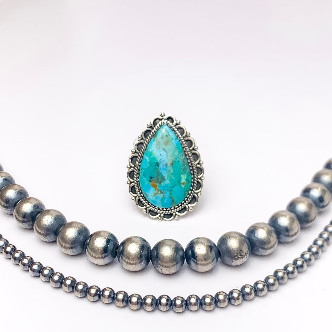 In the picture is a adjustable teardrop ring in kingman turquoise with a silver design around it with a white background