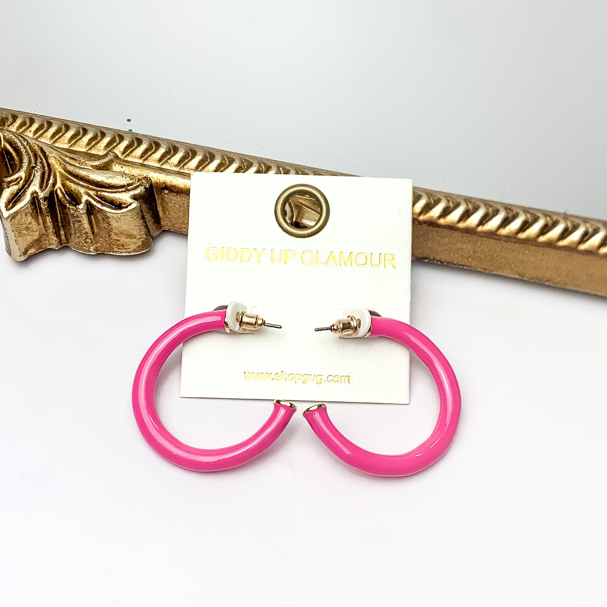 Plan For Cabo Small Hoop Earrings in Hot Pink. Pictured on a white background with a gold frame behind the earrings.