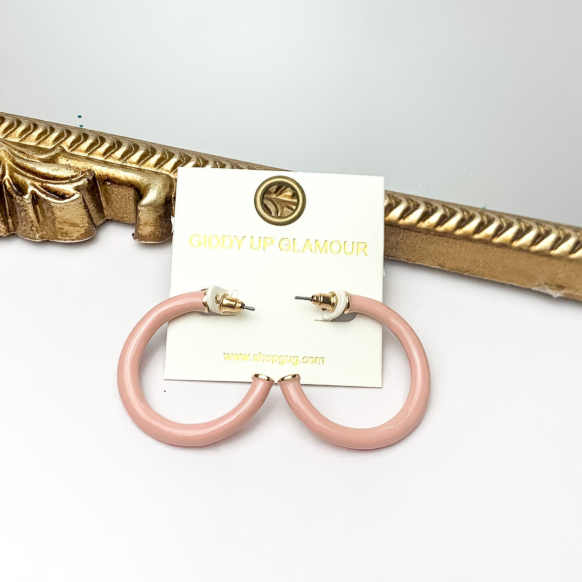 Plan For Cabo Small Hoop Earrings in Pale Pink. Pictured on a white background with a gold frame behind the earrings.