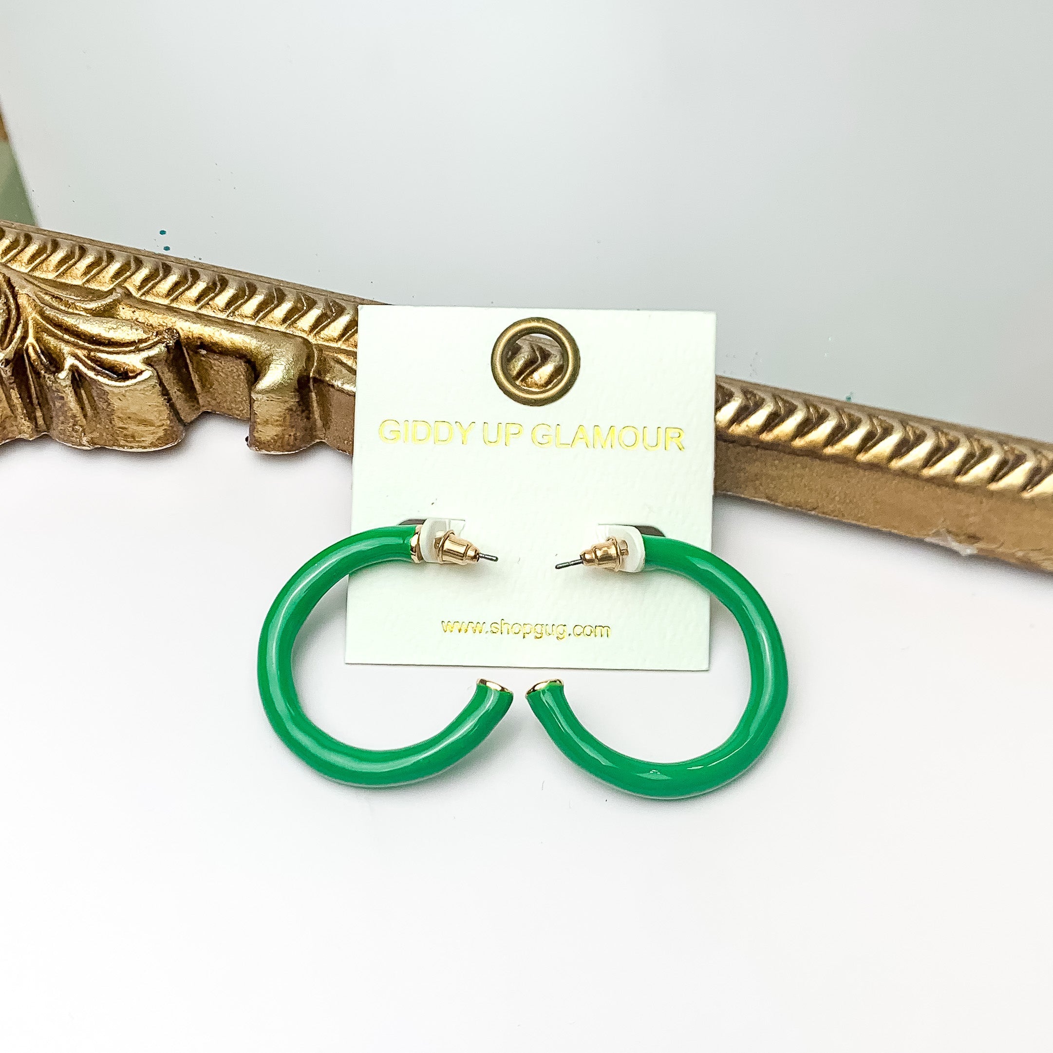 Plan For Cabo Small Hoop Earrings in Green. Pictured on a white background with a gold frame behind the earrings.