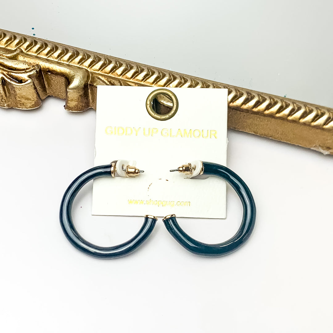 Plan For Cabo Small Hoop Earrings in Black. Pictured on a white background with a gold frame behind the earrings.