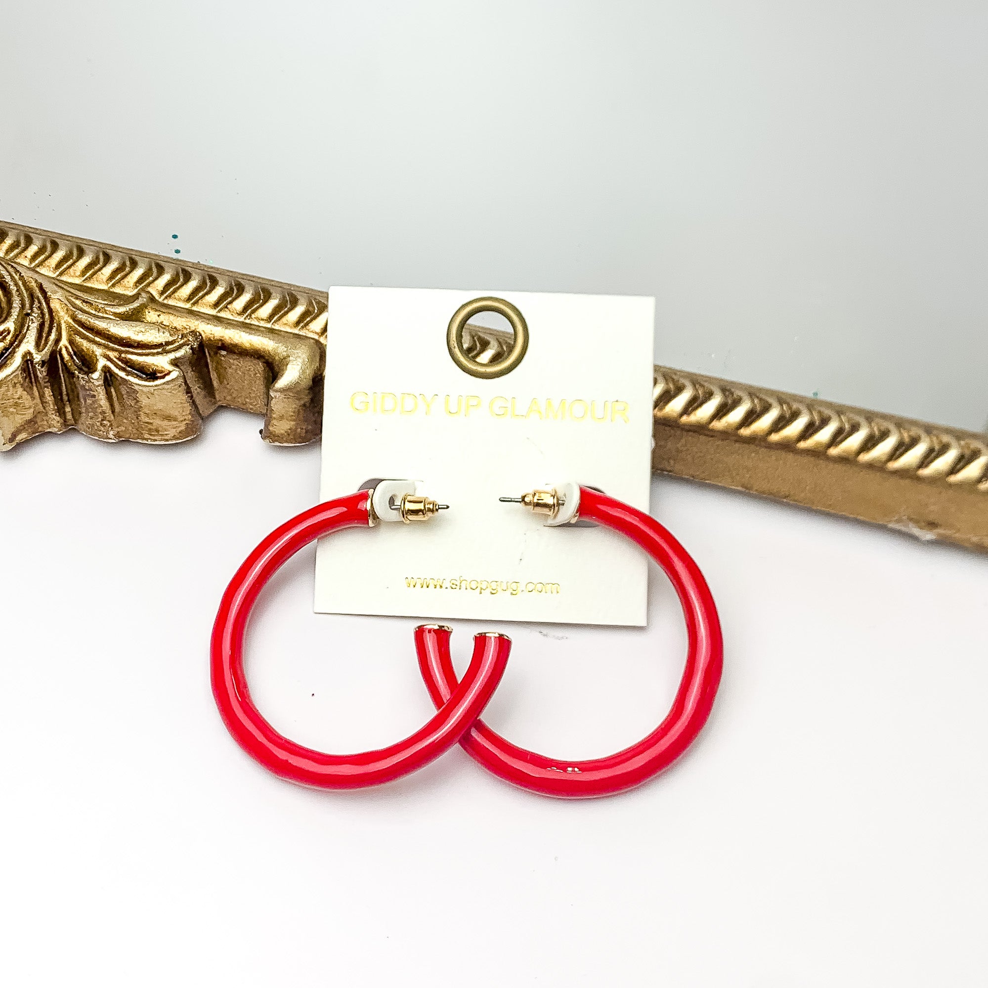 Plan For Cabo Large Hoop Earrings in Red. Pictured on a white background with a gold frame behind the earrings.