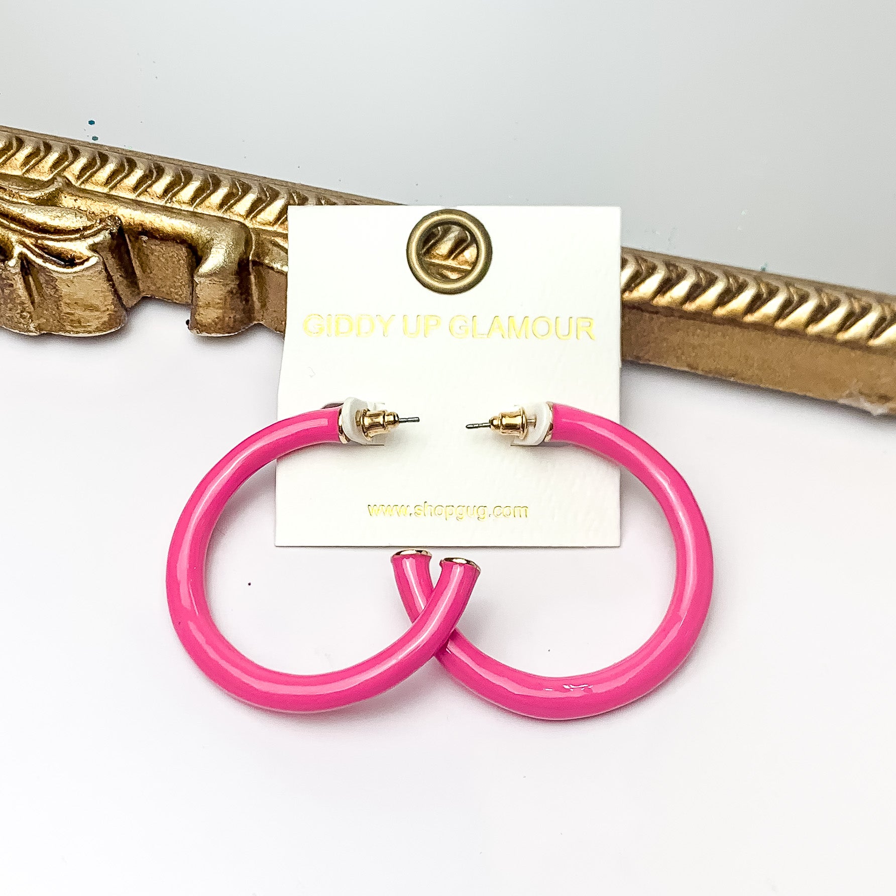 Plan For Cabo Large Hoop Earrings in Hot Pink. Pictured on a white background with a gold frame behind the earrings.