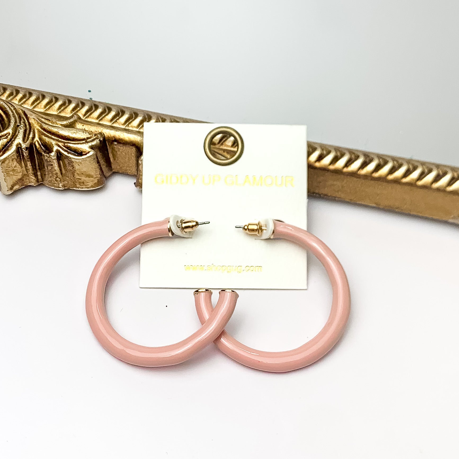Plan For Cabo Large Hoop Earrings in Pale Pink. Pictured on a white background with a gold frame behind the earrings.