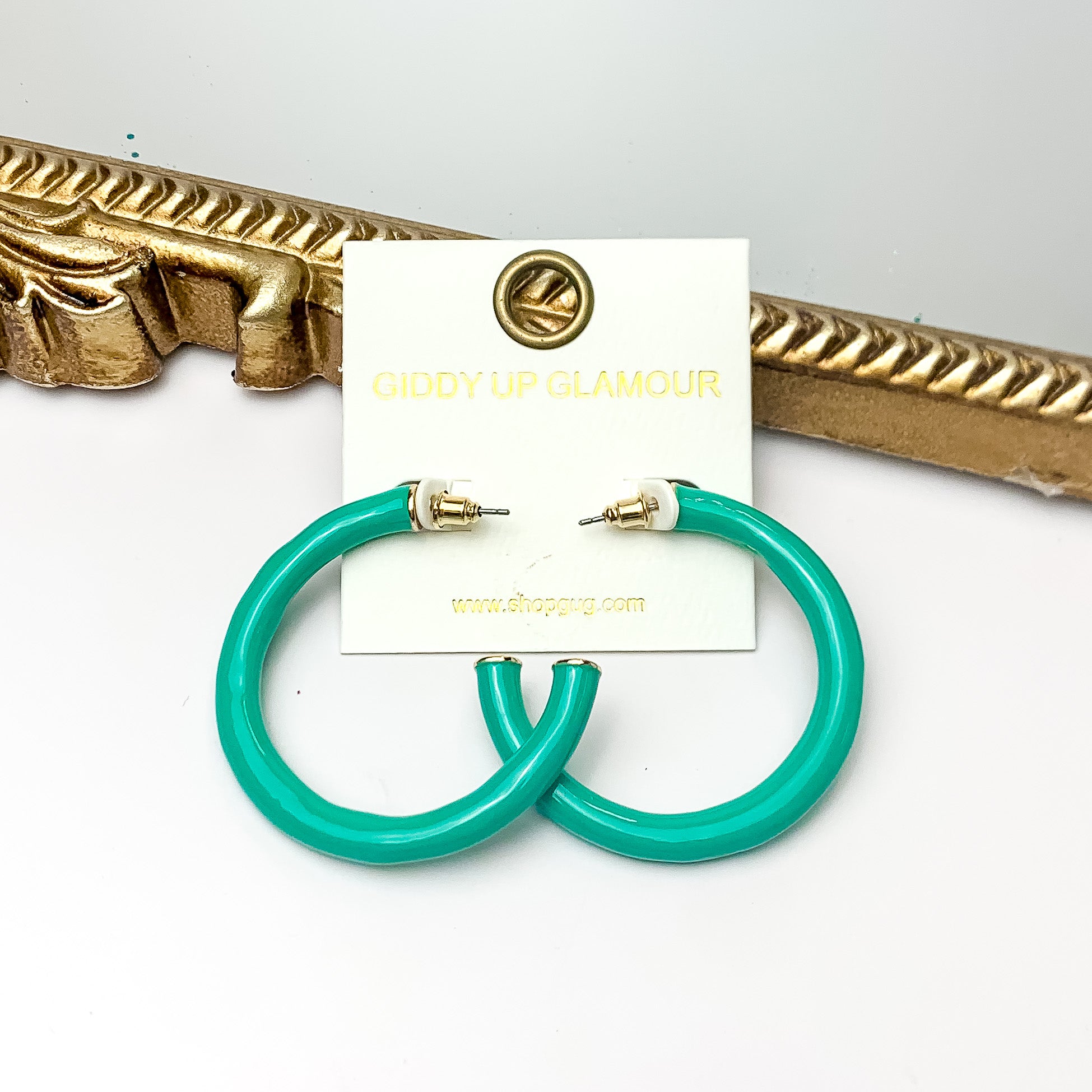 Plan For Cabo Large Hoop Earrings in Turquoise Green. Pictured on a white background with a gold frame behind the earrings.