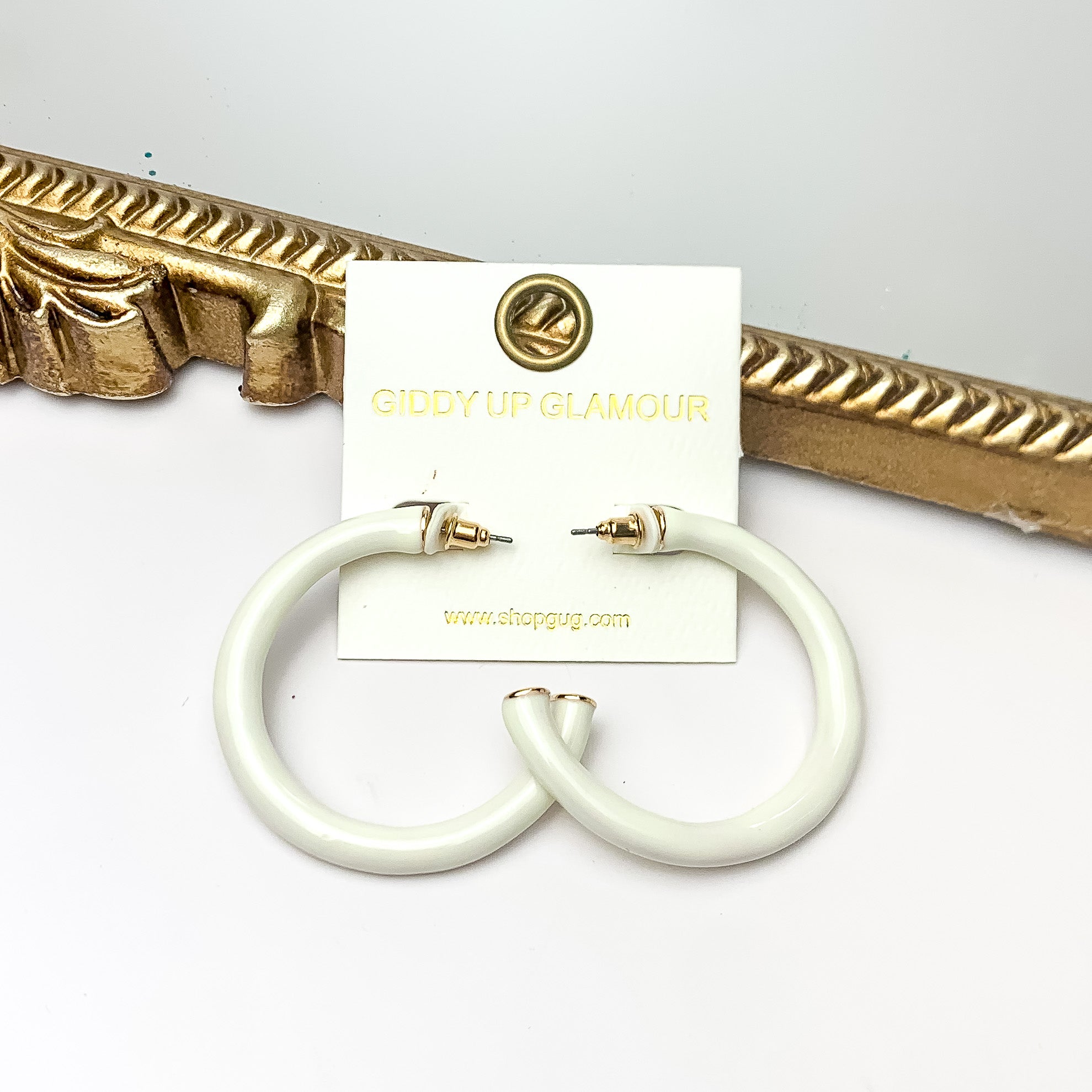 Plan For Cabo Large Hoop Earrings in Ivory. Pictured on a white background with a gold frame behind the earrings.