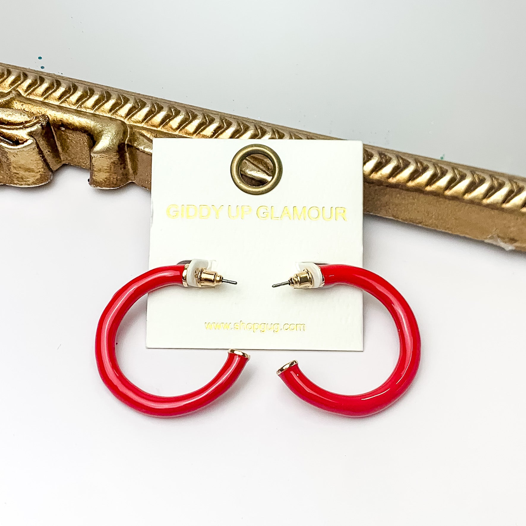 Plan For Cabo Small Hoop Earrings in Red. Pictured on a white background with a gold frame behind the earrings.