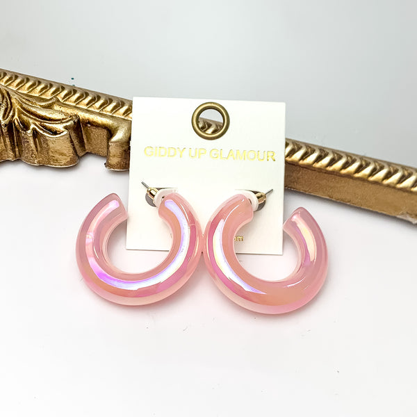 Pictured is a pair of chunky tube hoop earrings in iridescent pink. These earrings are pictured on a white background with a gold mirror behind them. 