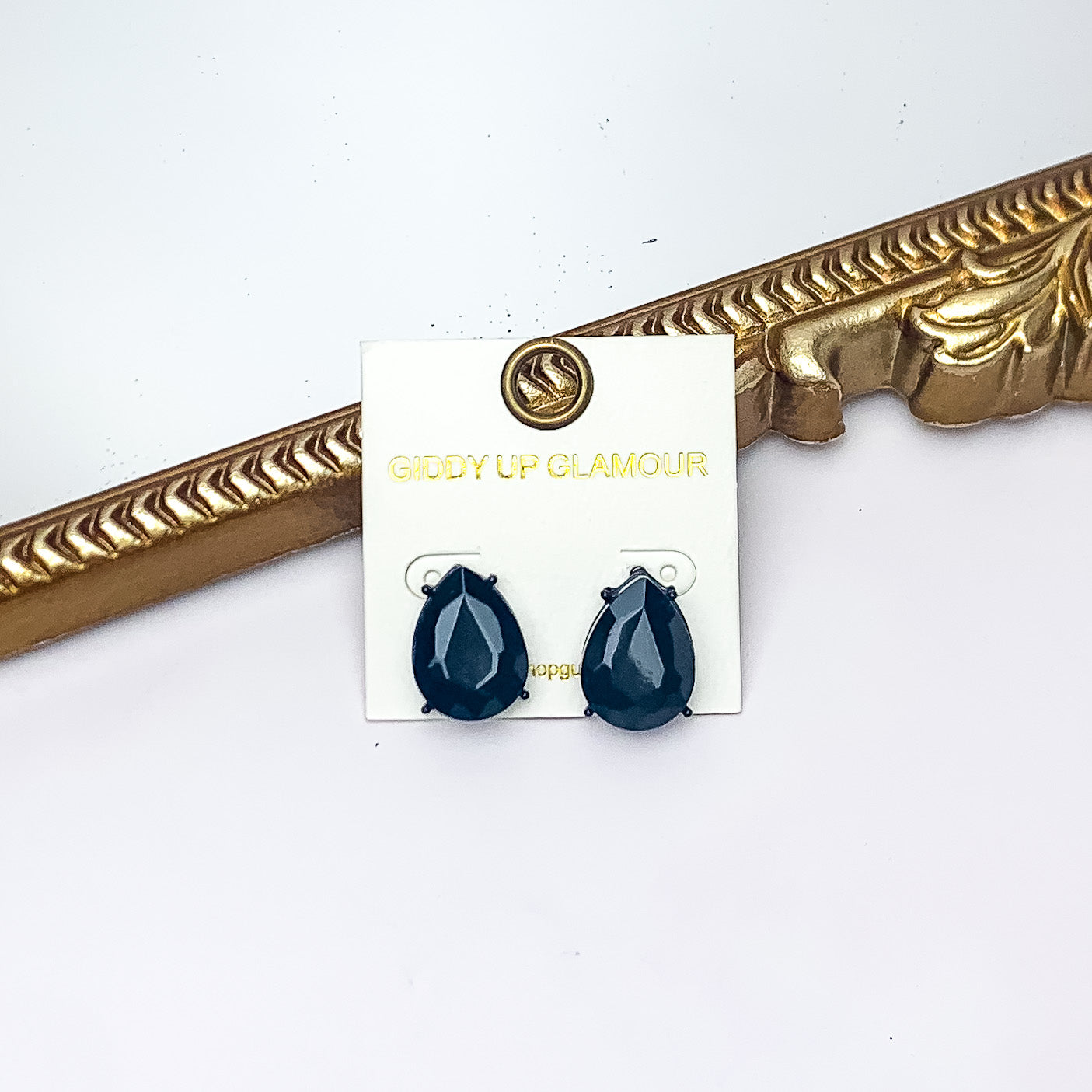 Teardrop Stud Earrings With Crystals in Black. Pictured on a white background with a gold frame behind the earrings.