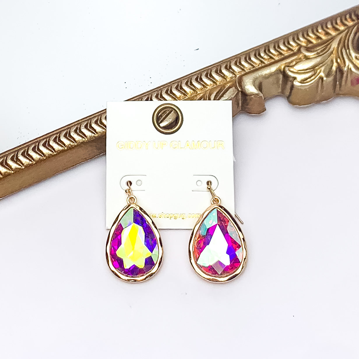 Gold Tone Large Teardrop Earrings With AB Crystals. Pictured on a white background with a gold frame behind the earrings.