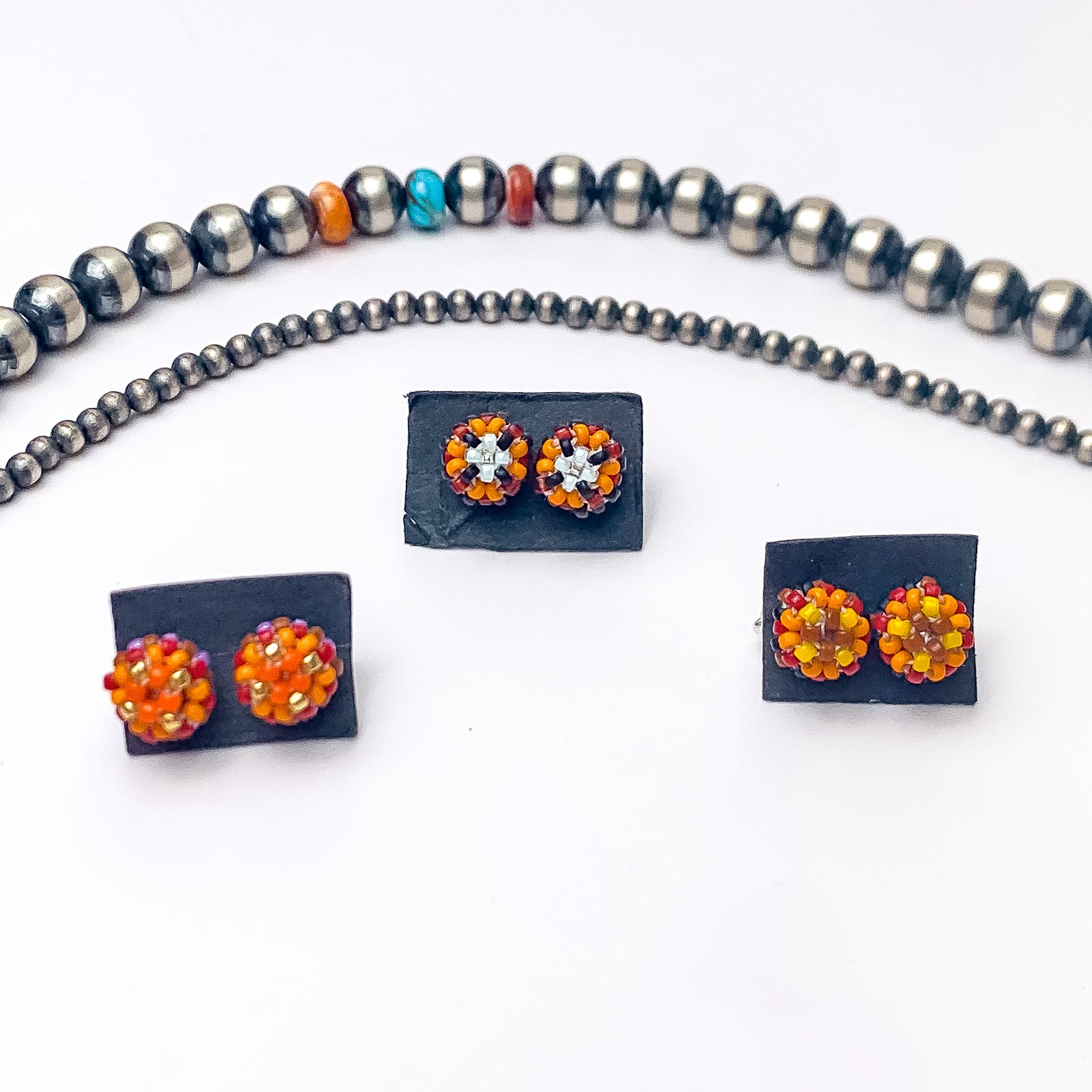 Pictured are four pairs of circle, beaded stud earrings in a mix of orange beads that are different in each pair. These earrings are pictured on a white background with silver beads above the studs. 