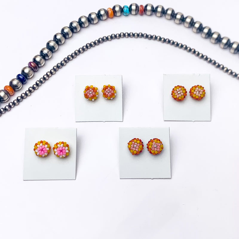 Pictured are four pairs of circle, beaded stud earrings in a mix of orange and pink beads that are different in each pair. These earrings are pictured on a white background with silver beads above the studs.