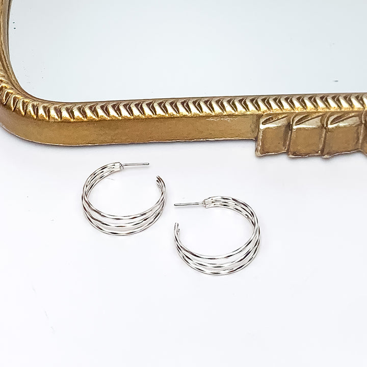 Good Karma Medium Triple Hoop Earrings in Silver Tone. Pictured on a white background with a gold frame above the earrings.