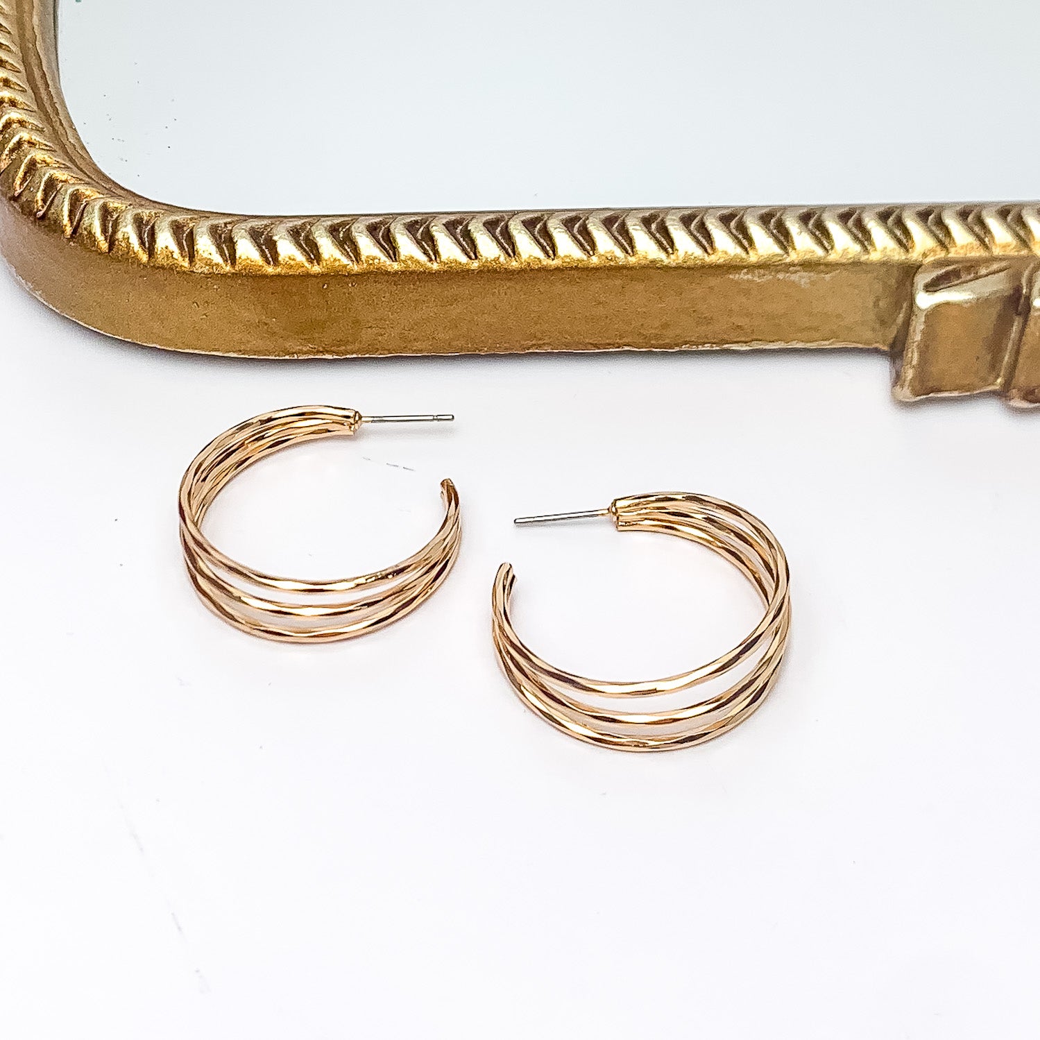 Good Karma Medium Triple Hoop Earrings in Gold Tone. Pictured on a white background with a gold frame above the earrings.