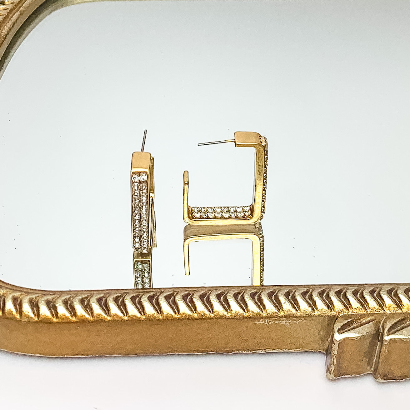 Gold Tone Rectangle Hoop Earrings With Clear Crystal Inlay. Pictured on a mirror with a gold trim.