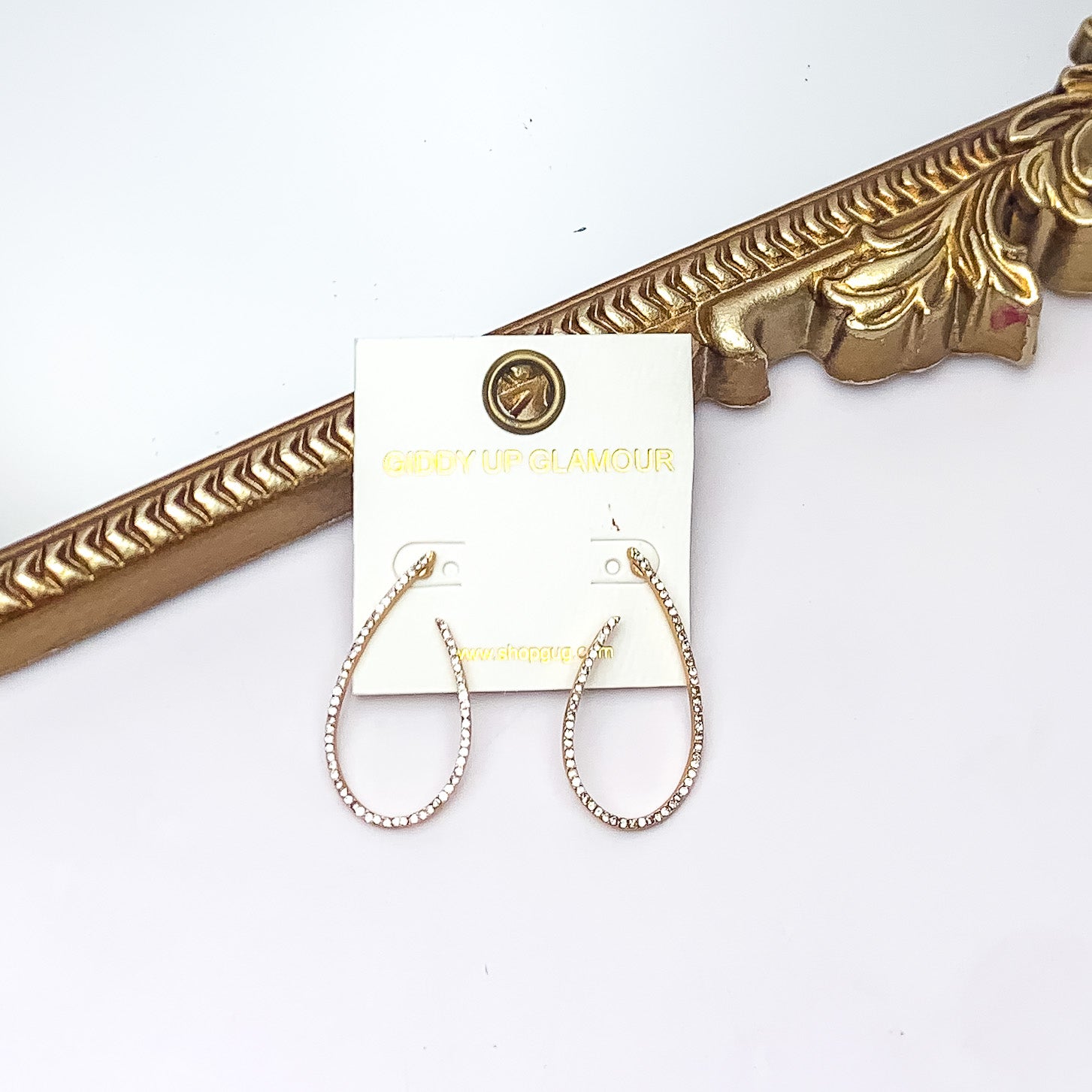 Classy and Confident Open Teardrop Earrings With Clear Crystals in Gold Tone. Pictured on a white background with a gold frame behind the earrings. 