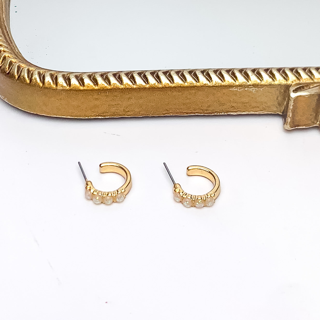 Small Gold Tone Hoop Earrings With Opal Stones. Pictured on a white background with a gold frame above the earrings.