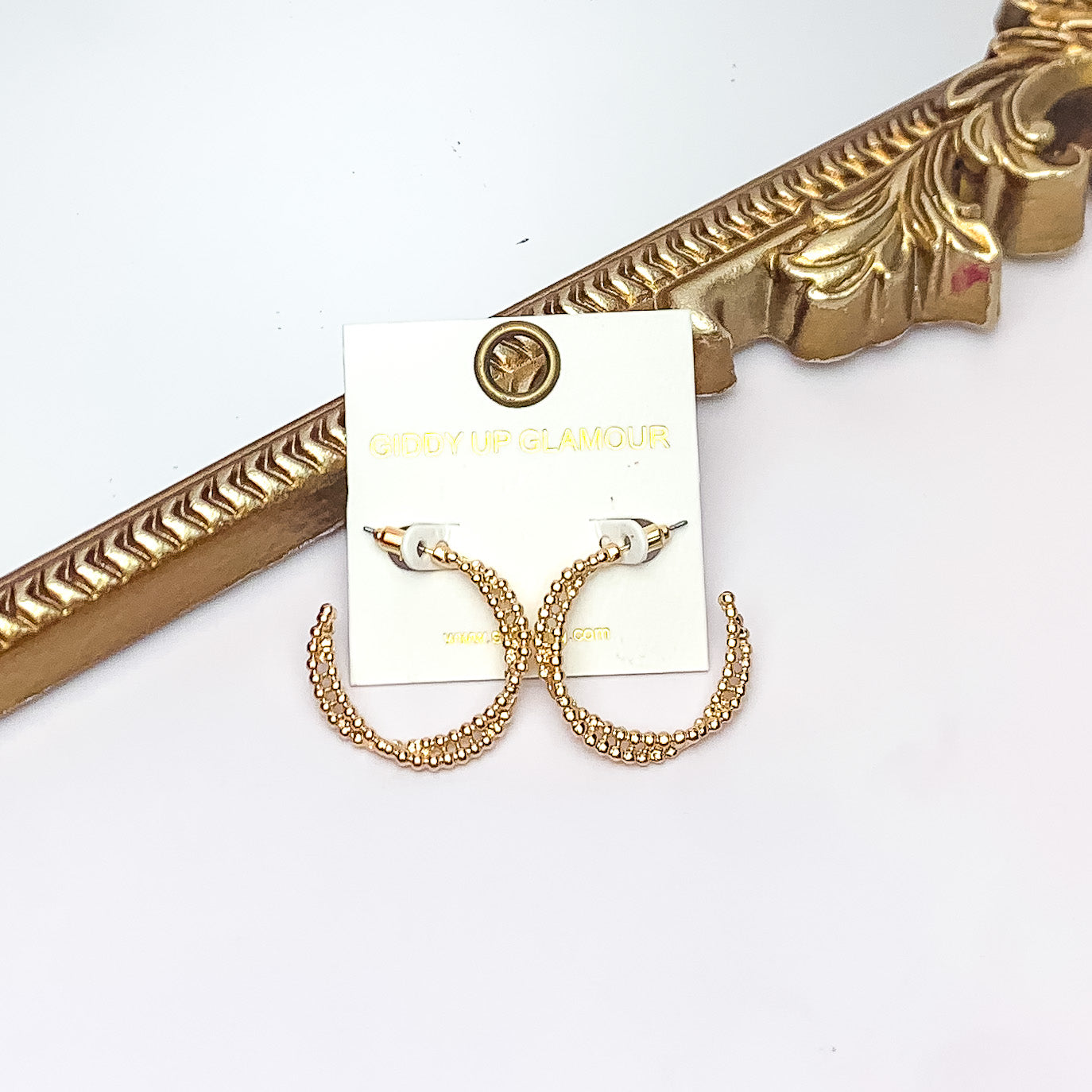 Everyday Glam Double Twisted Hoop Earrings in Gold Tone. Pictured on a white background with a gold frame behind the earrings.