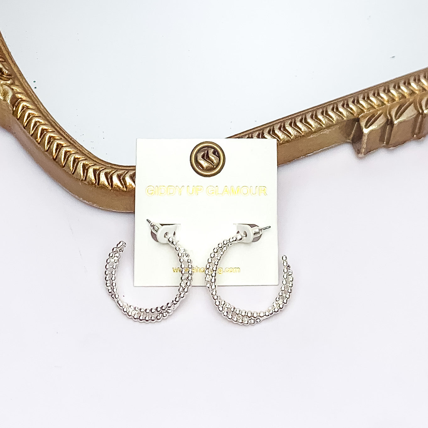 Everyday Glam Double Twisted Hoop Earrings in Silver Tone. Pictured on a white background with a gold frame behind the earrings.
