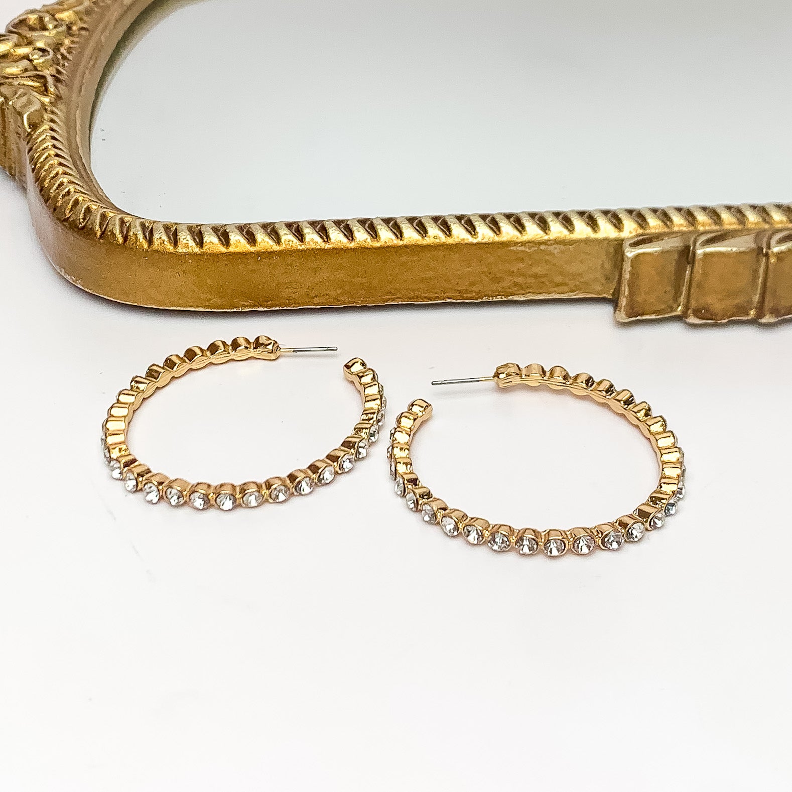 Large Gold Tone Hoop Earrings Outlined in Clear Crystals. Pictured on a white background with a gold frame above the earrings.
