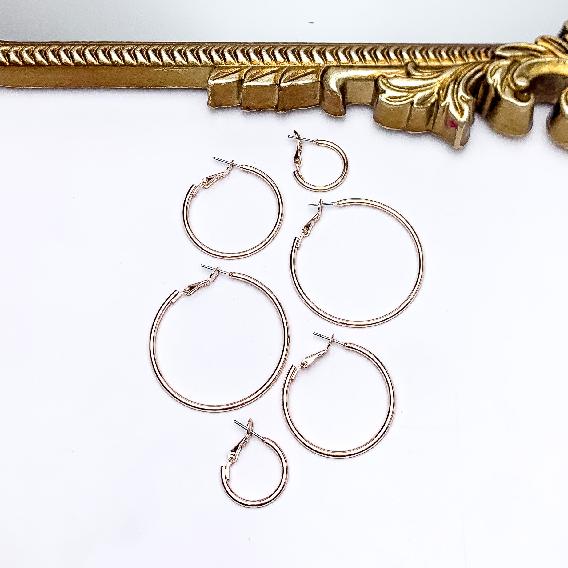 Set Of Three | Hoop Earrings in Rose Gold Tone. Pictured on a white background with a gold frame above the earrings. There are three different sizes of earrings all in the picture.