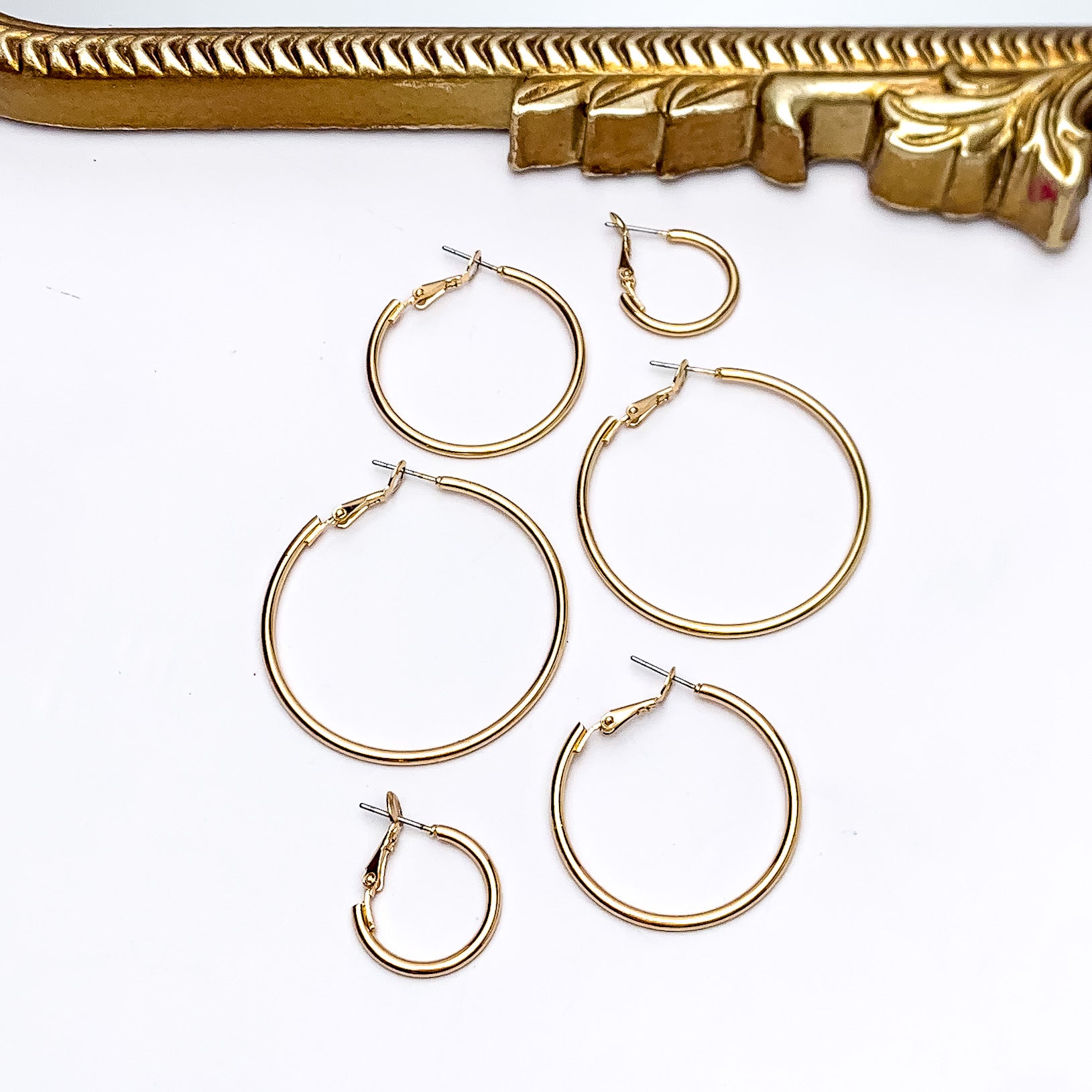 Set Of Three | Hoop Earrings in Gold Tone. Pictured on a white background with a gold frame above the earrings. There are three different sizes of earrings all in the picture.