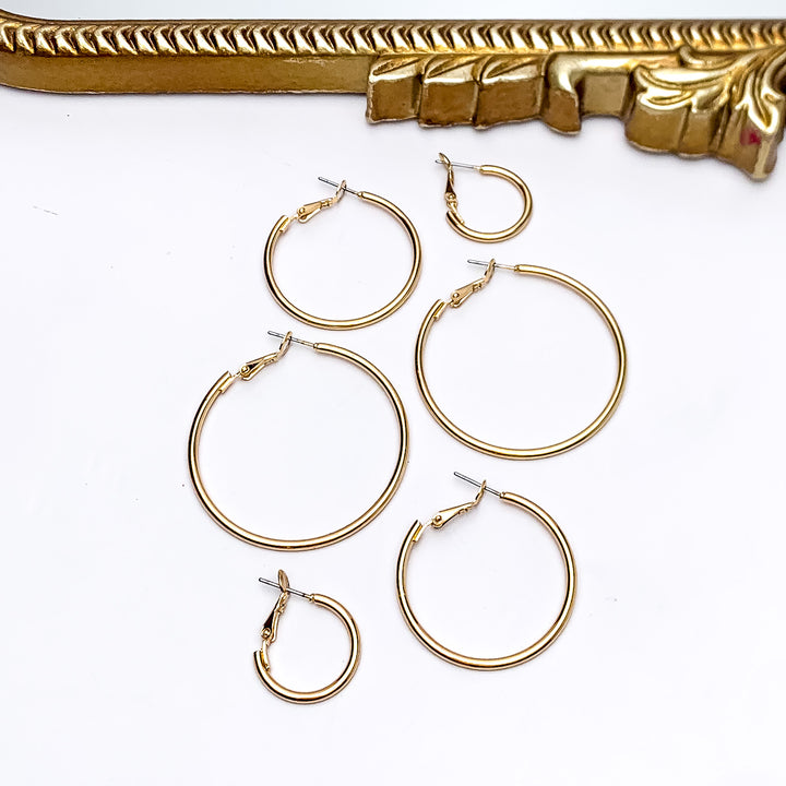 Set Of Three | Hoop Earrings in Gold Tone. Pictured on a white background with a gold frame above the earrings. There are three different sizes of earrings all in the picture.