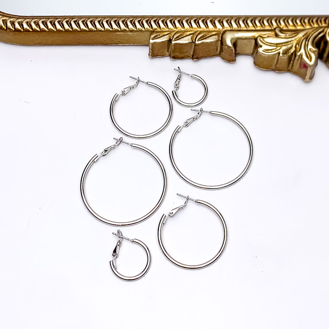 Set Of Three | Hoop Earrings in Silver Tone. Pictured on a white background with a gold frame above the earrings. There are three different sizes of earrings all in the picture.