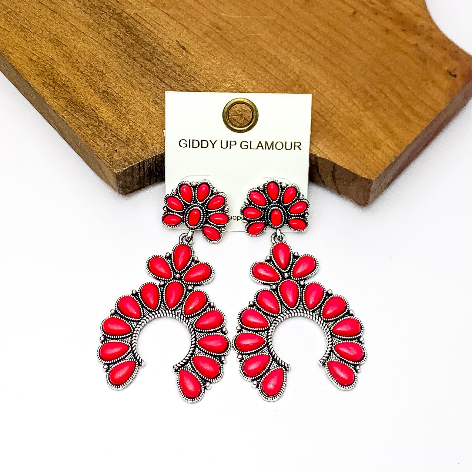 Western Naja Earrings in Silver Tone with Red Stones. Pictured on a white background with a wood piece behind the earrings.